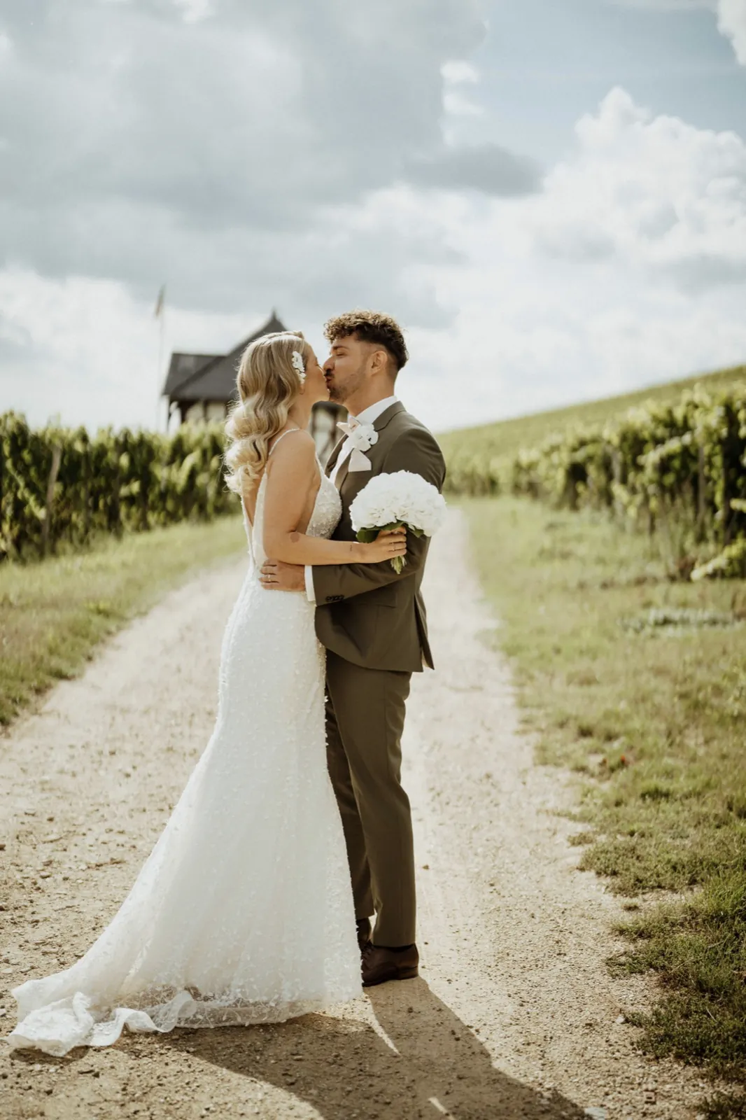 Luisa & Norman – Ein Brautpaar küsst sich auf einem Feldweg inmitten von Weinbergen