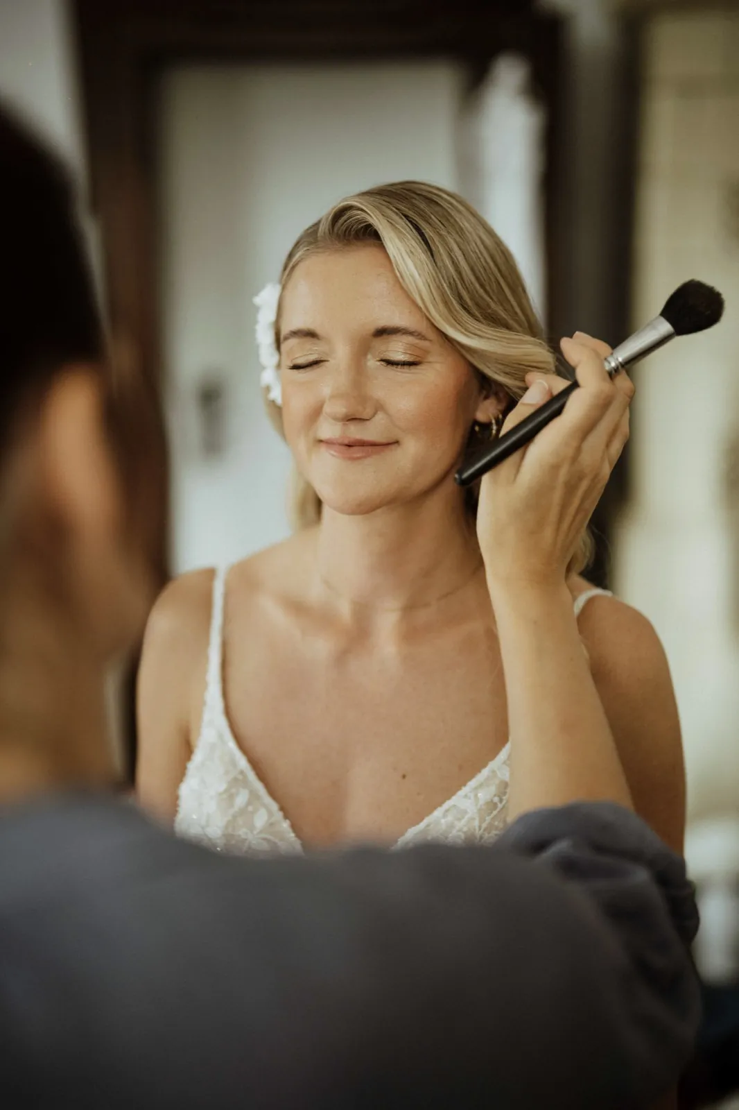 Luisa & Norman – Eine Braut schließt lächelnd die Augen, während ihr Make-up aufgetragen wird