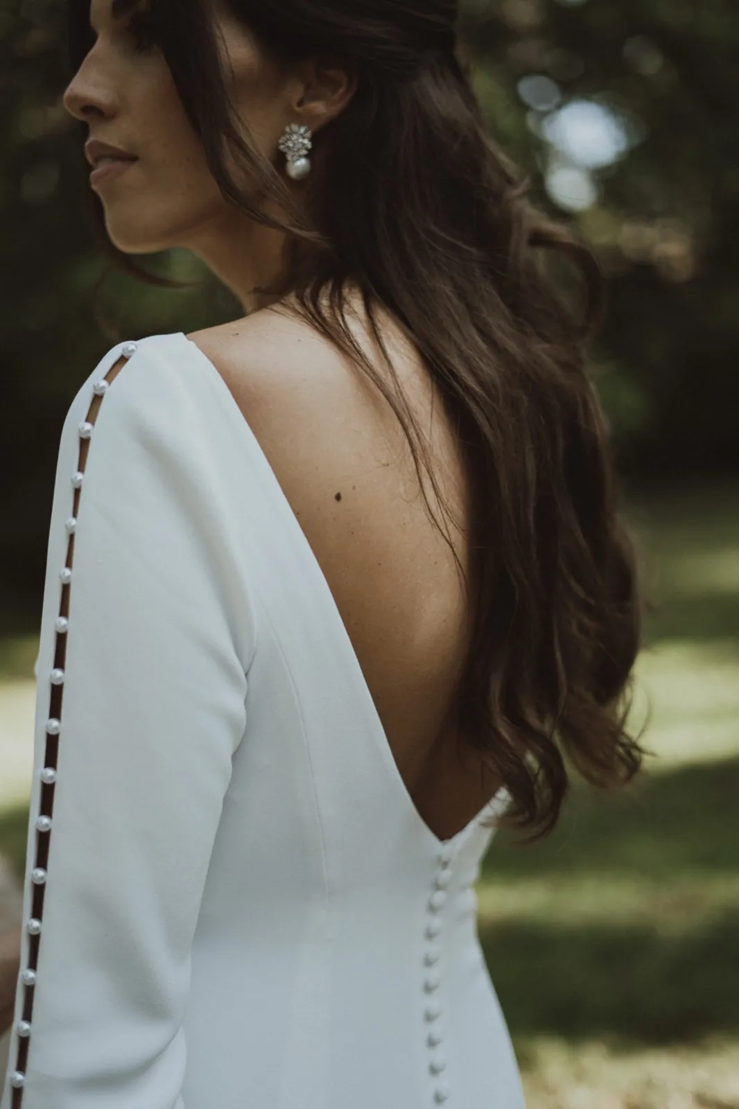 Clarissa & Kai – Rückansicht einer Braut im weißen Hochzeitskleid mit Perlenknöpfen im Freien