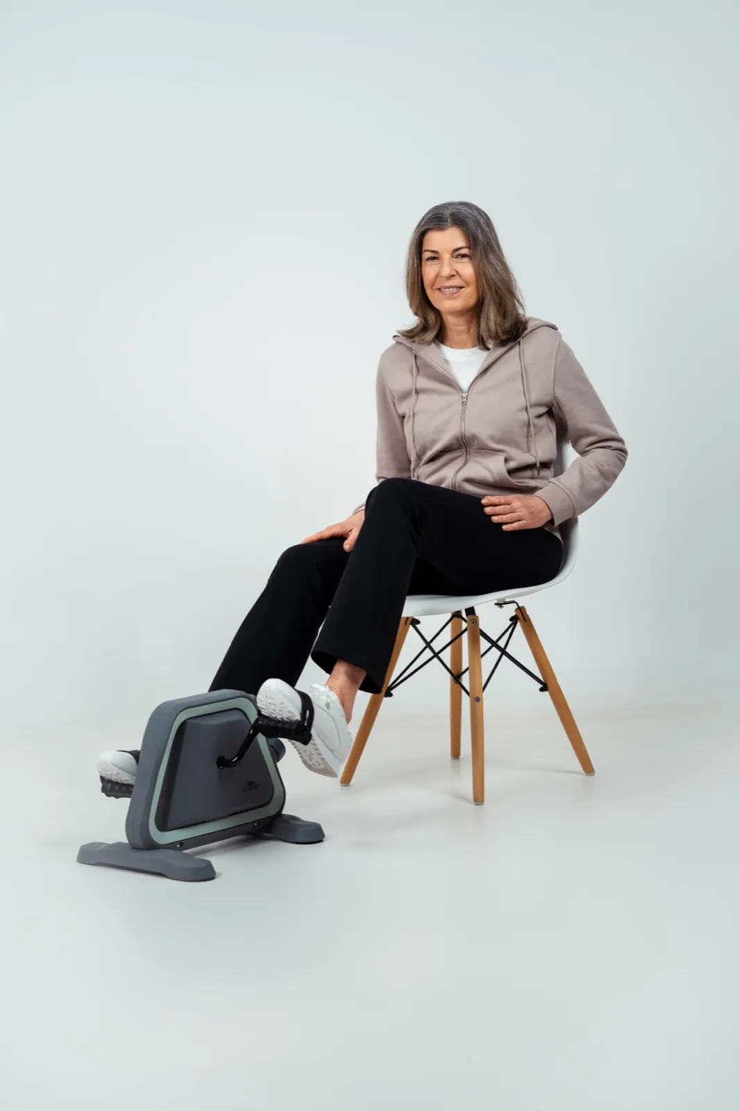 ALDI – Eine ältere Frau sitzt auf einem Stuhl und benutzt einen Pedaltrainer im Studio