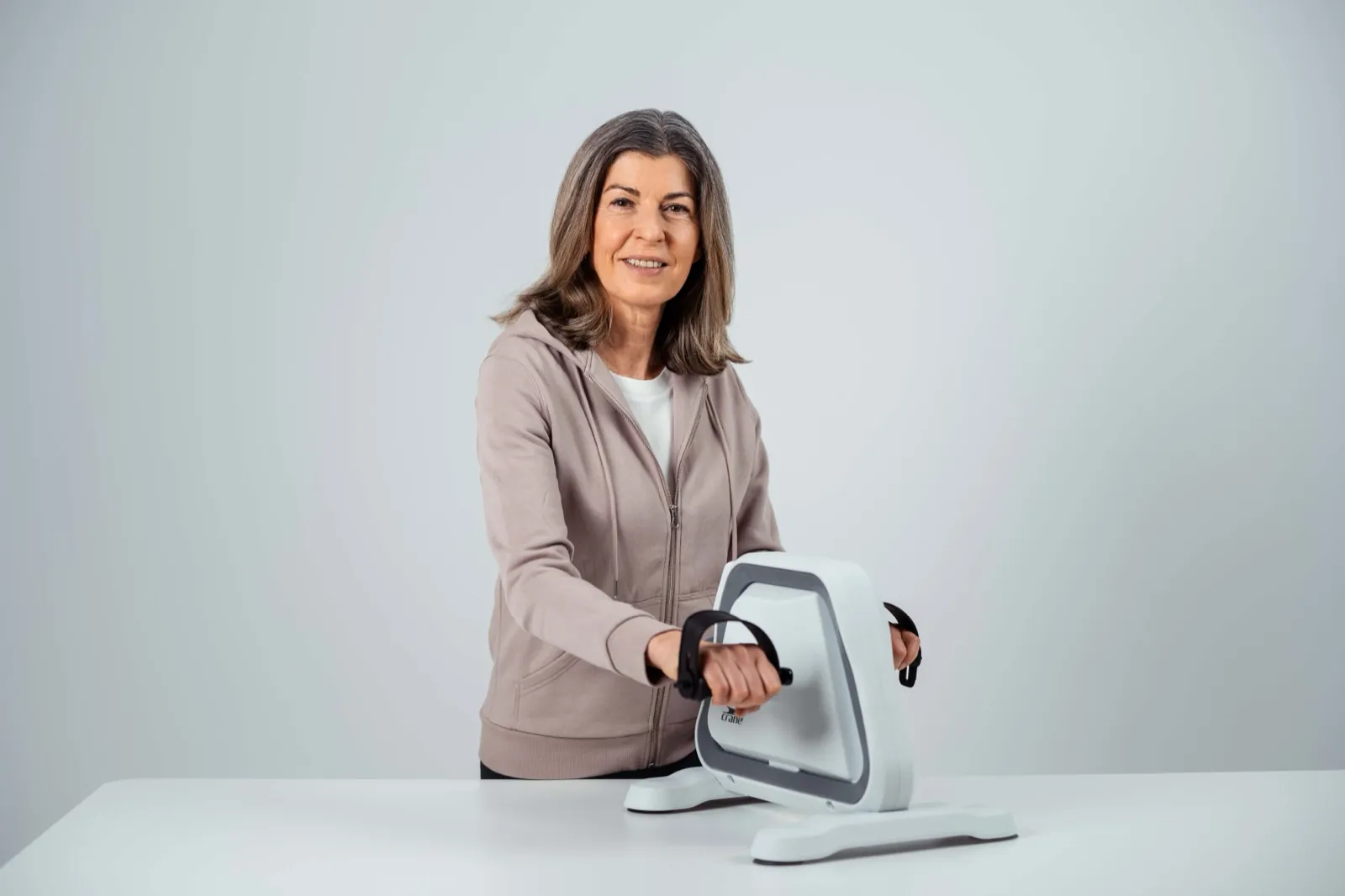 ALDI – Eine ältere Frau lächelt im Studio, während sie ein Handpedal-Trainingsgerät benutzt