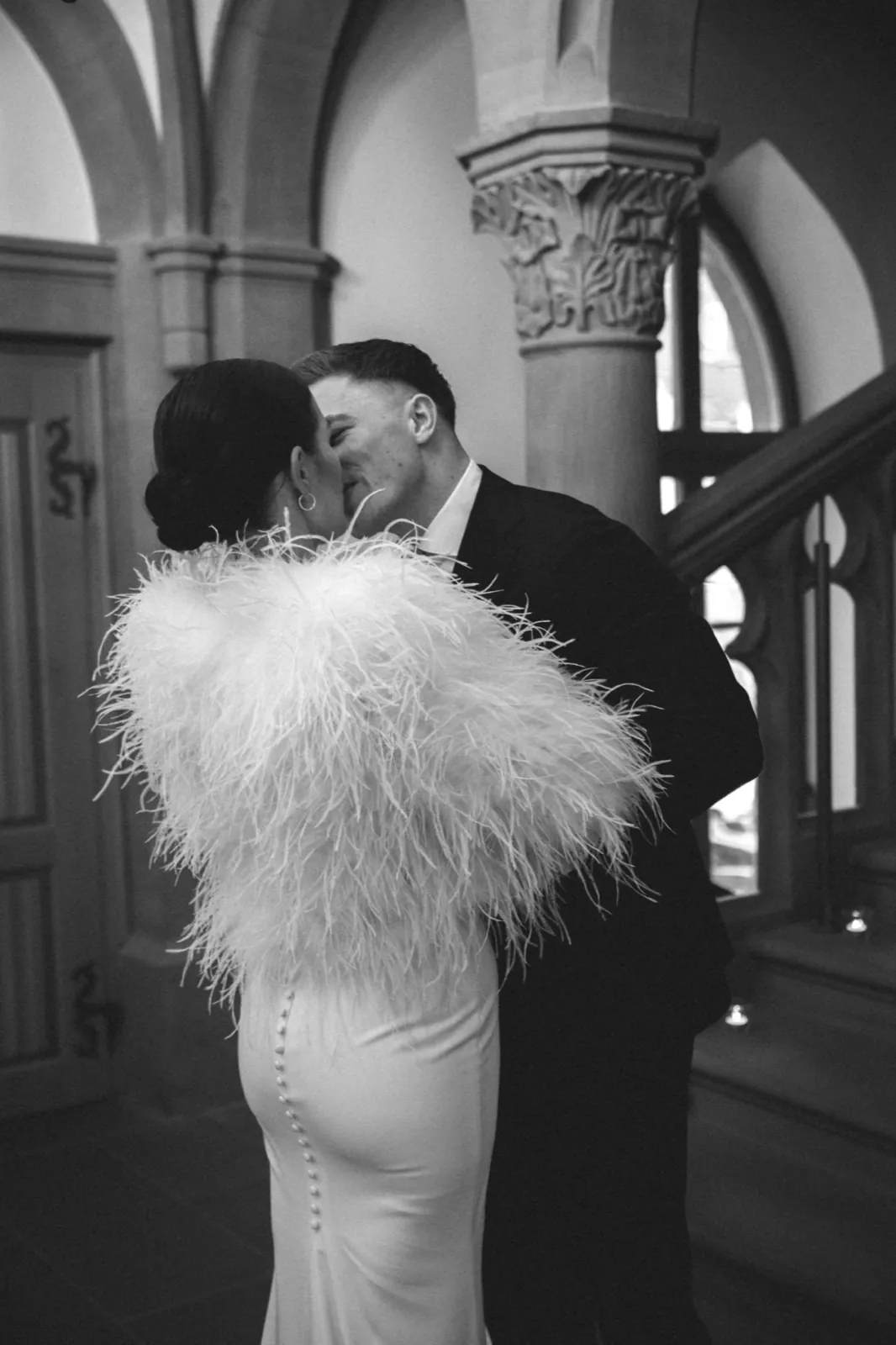 Alisa & Lars – Ein Brautpaar küsst sich innig in einem historischen Gebäude in Schwarz-Weiß