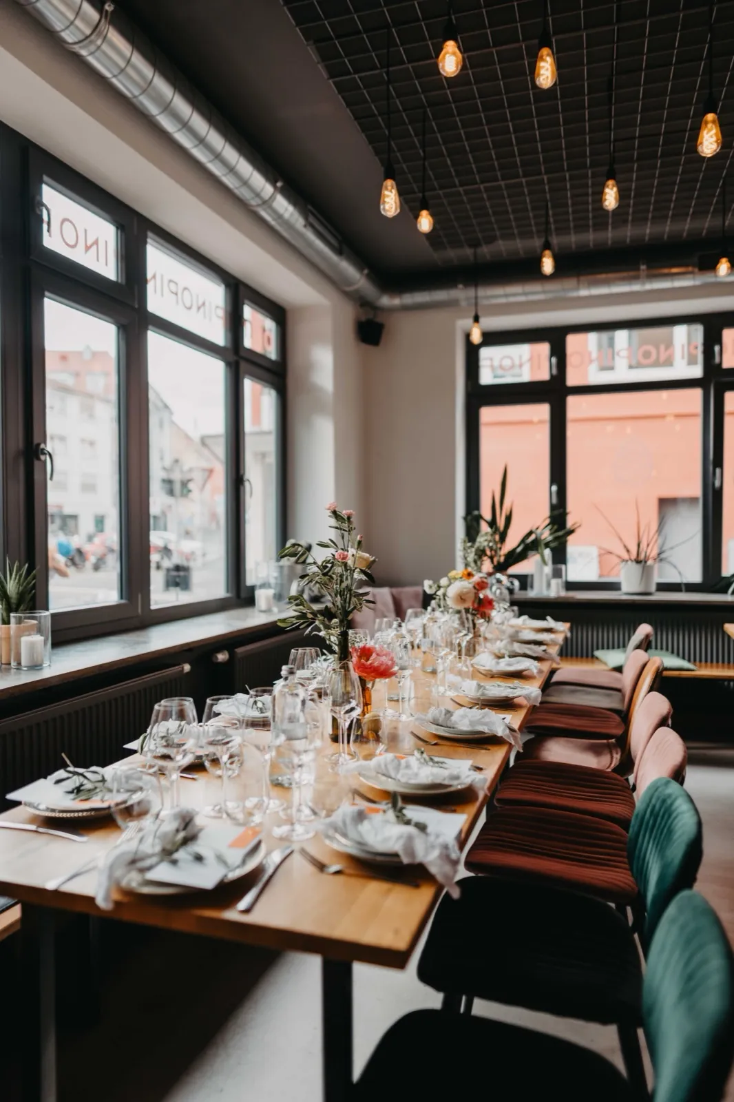 Amelie & Andi – Ein festlich gedeckter langer Holztisch mit Gläsern und Blumen in einem modern gestalteten Restaurant