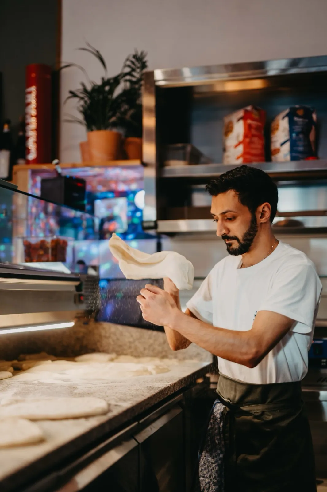 Amelie & Andi – Ein Bäcker wirft Pizzateig in einer professionellen Küche in die Luft