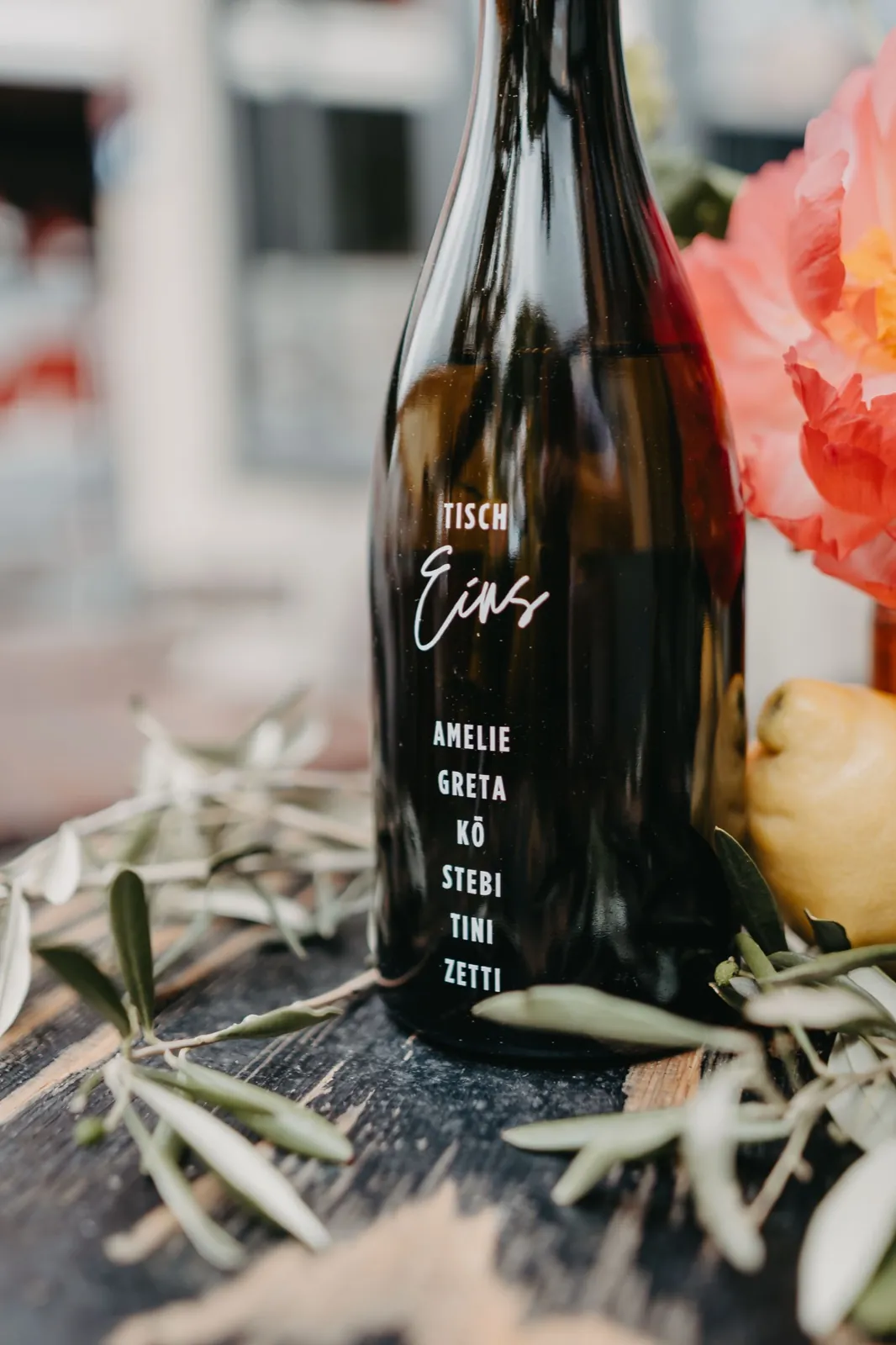 Amelie & Andi – Eine dunkle Flasche mit weißer Aufschrift dient als Tischkarte bei einer Hochzeit