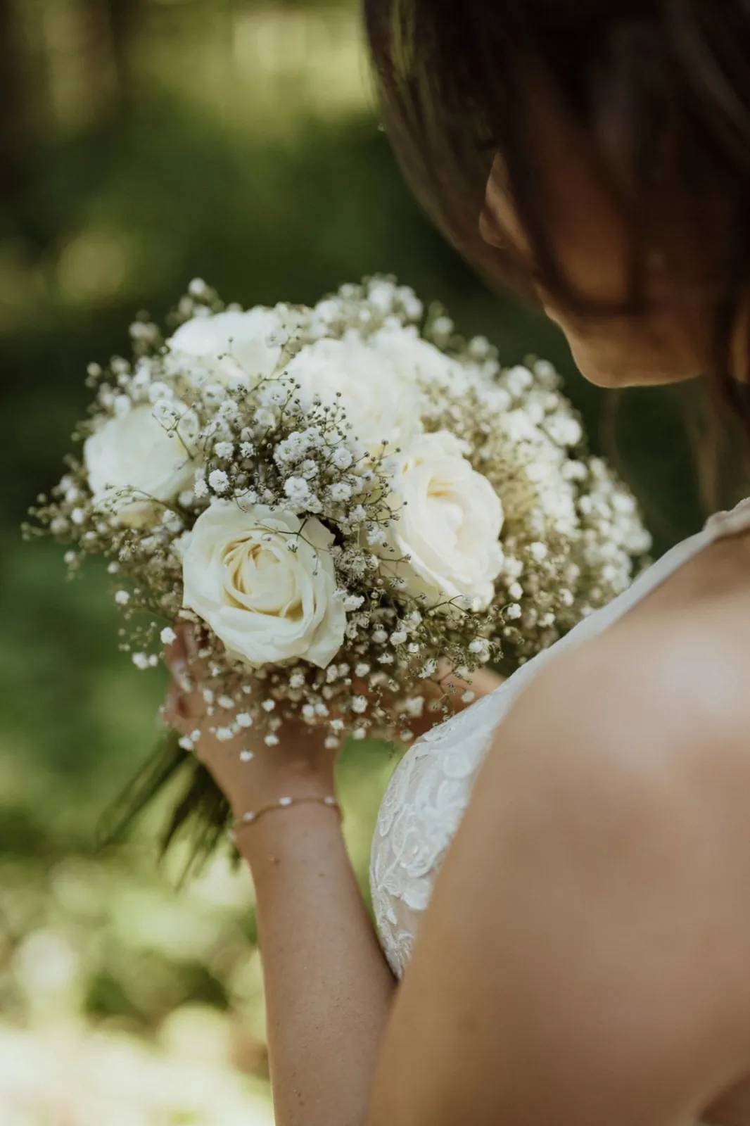 Anna & Moritz – Eine Braut hält einen weißen Brautstrauß aus Rosen und Schleierkraut im Freien