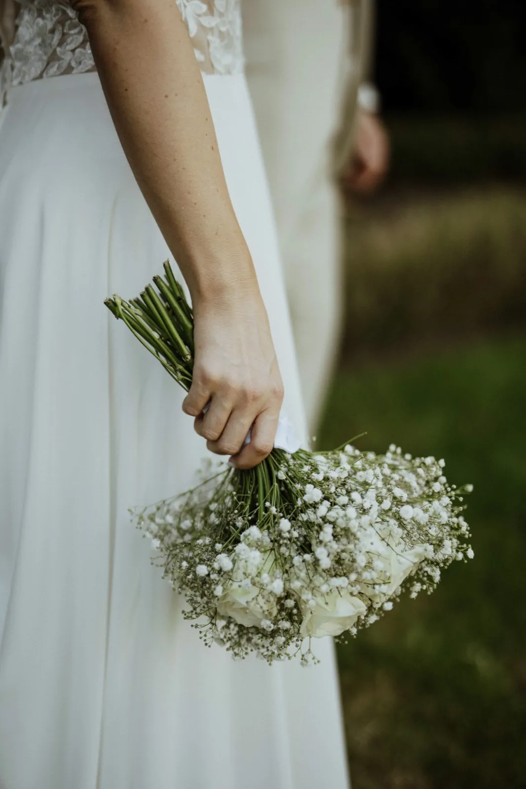 Anna & Moritz – Eine Braut hält einen Brautstrauß aus Schleierkraut und weißen Rosen in der Hand