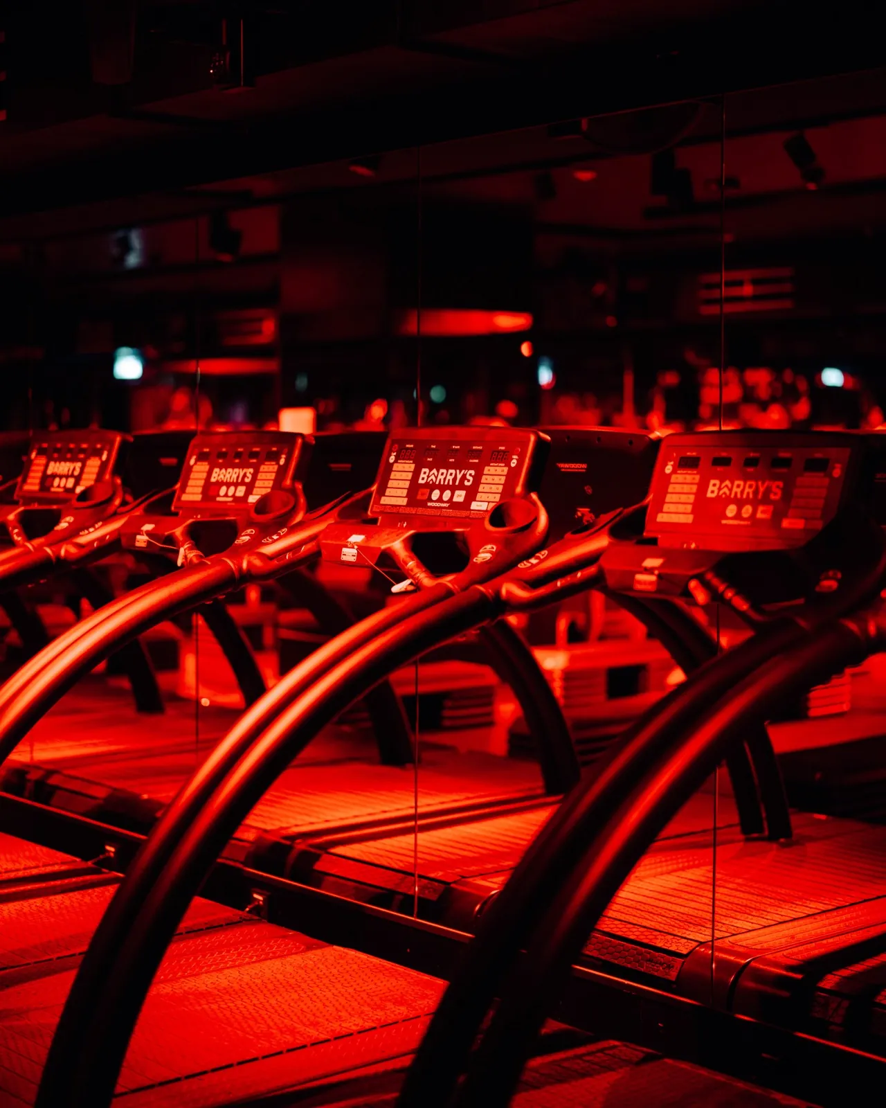 Barry's Frankfurt – Eine Reihe von Laufbändern in einem Fitnessstudio mit intensiver roter Beleuchtung