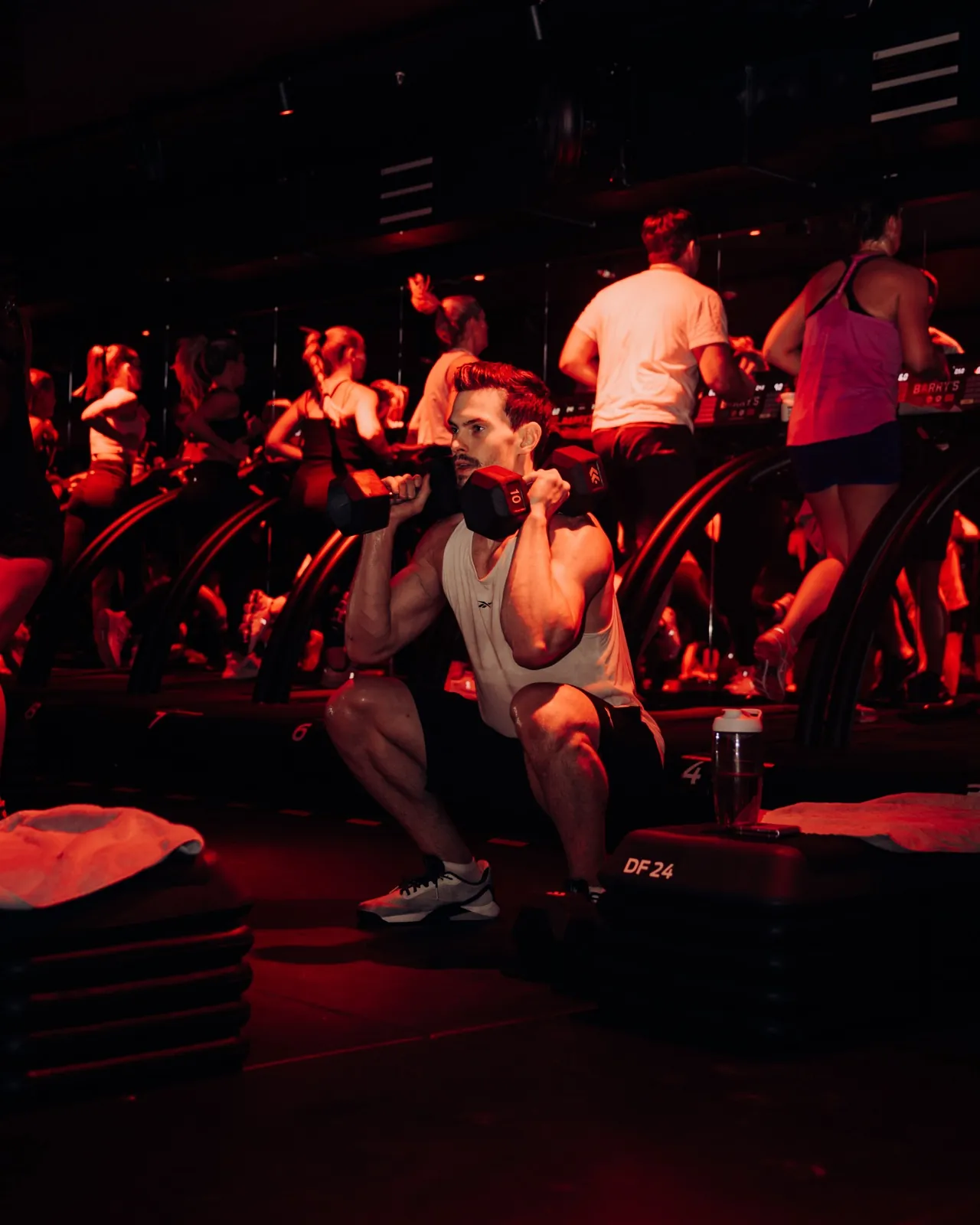 Barry's Frankfurt – Ein Mann macht Kniebeugen mit Hanteln in einem rot beleuchteten Fitnessstudio