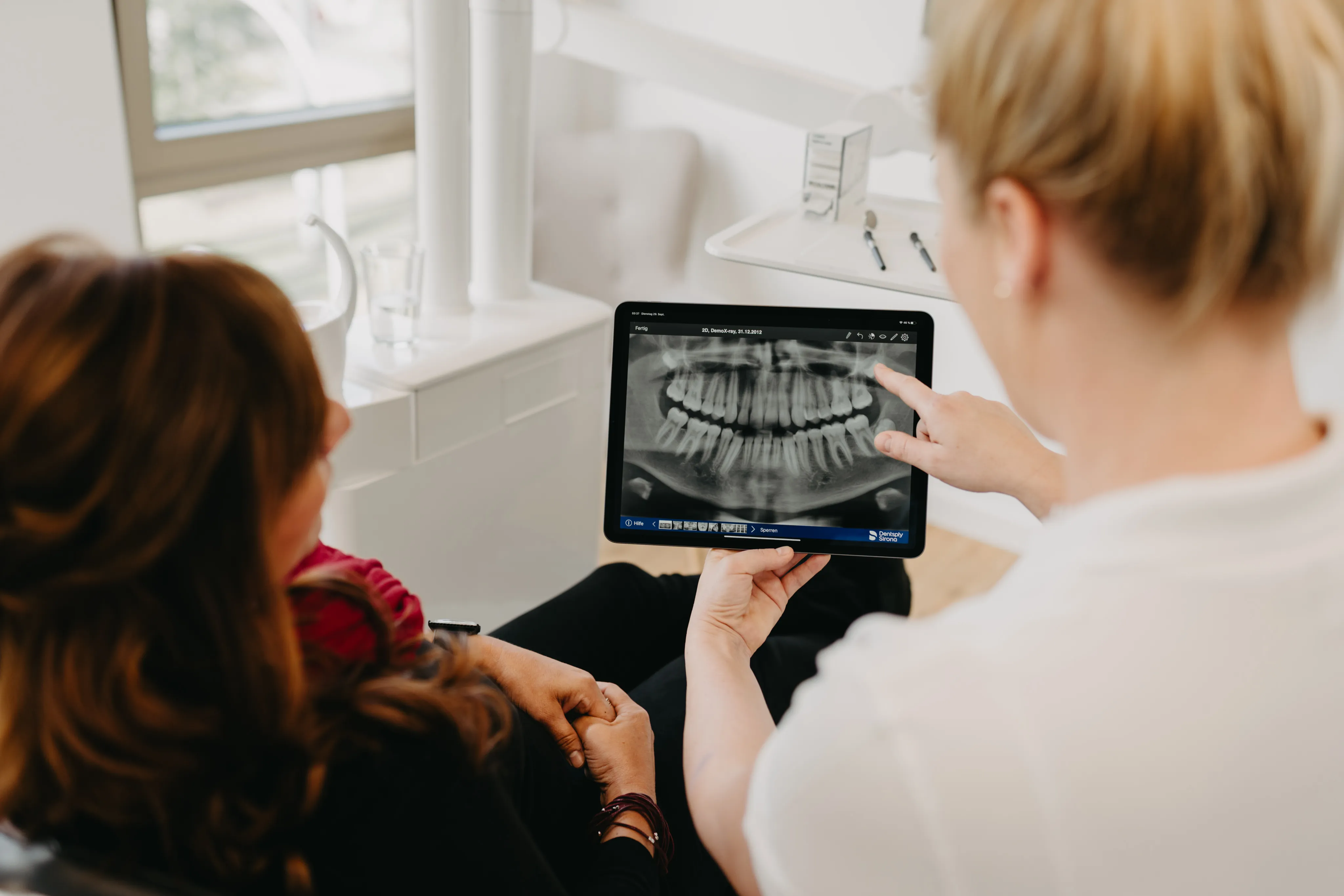 Bünger & Meißner – Eine Zahnärztin zeigt einer Patientin ein Röntgenbild der Zähne auf einem Tablet