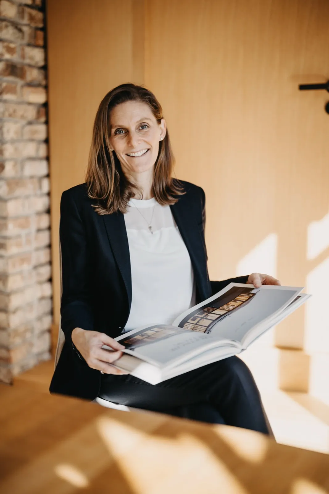 Franziska Hildenbrandt – Eine lächelnde Frau im Business-Outfit sitzt drinnen und hält ein geöffnetes Buch