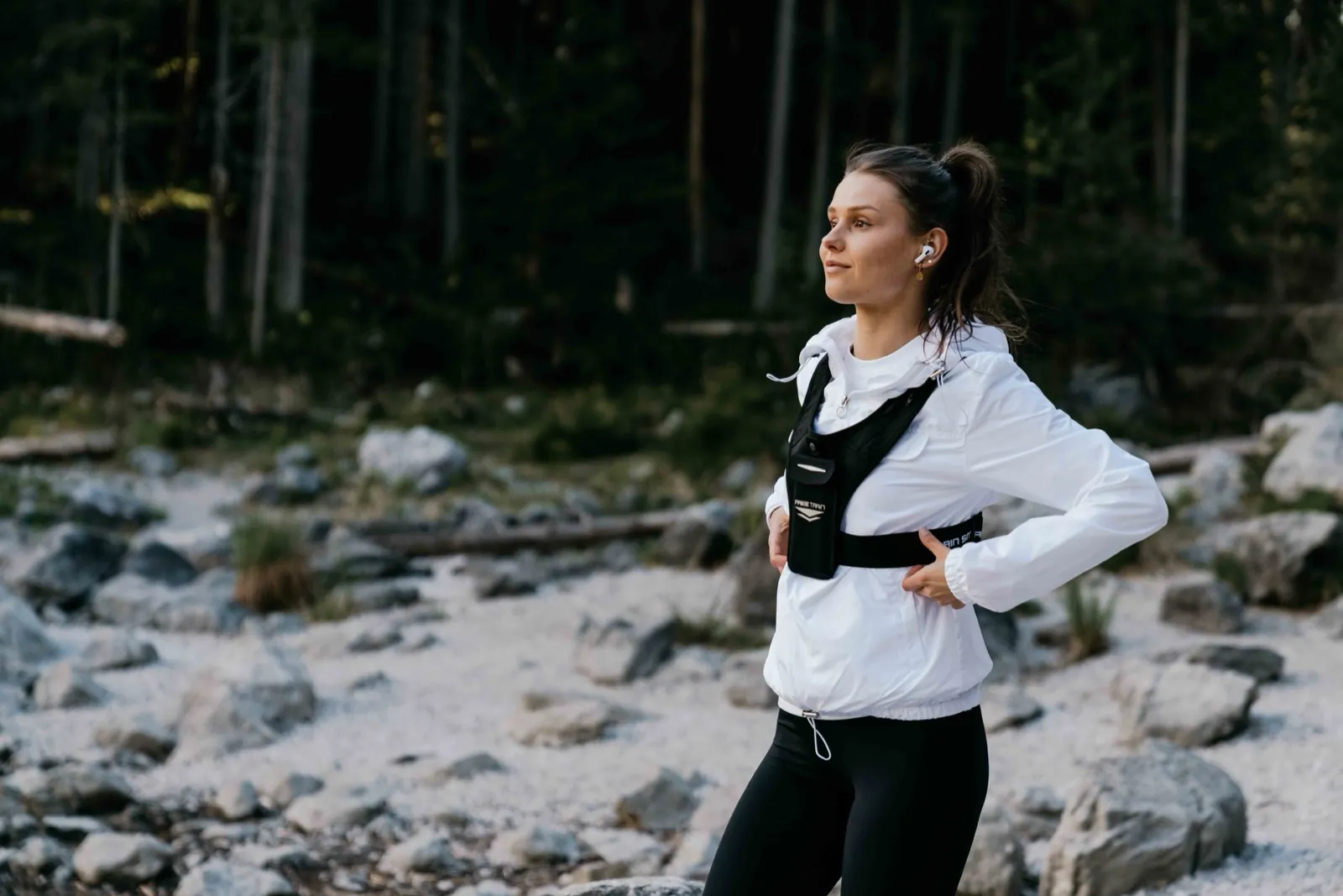 Freetrain – Eine sportliche Frau steht in Laufbekleidung und einer Weste in einer steinigen Waldlandschaft