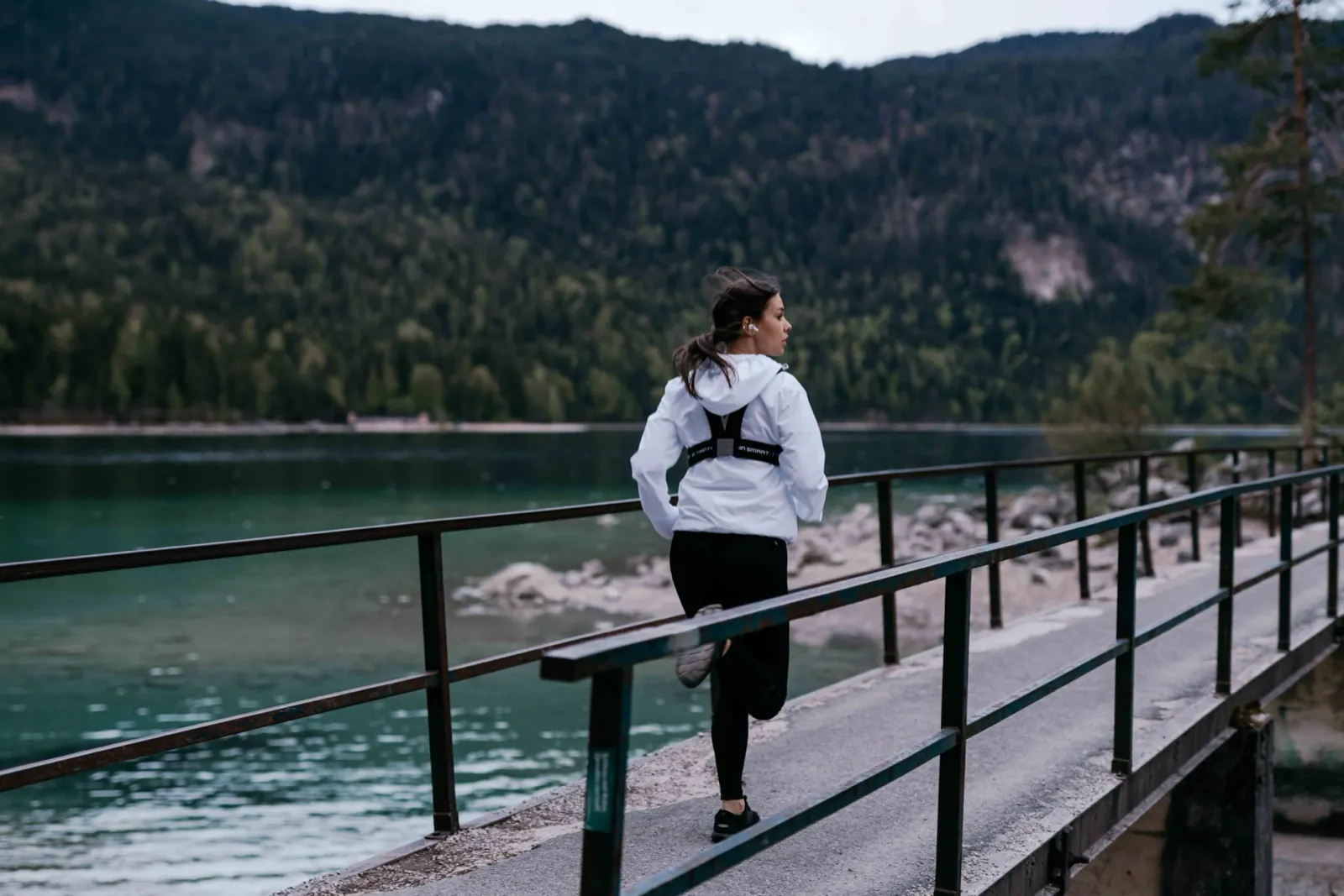 Freetrain – Eine Frau joggt auf einem Steg an einem Bergsee vor bewaldeten Bergen