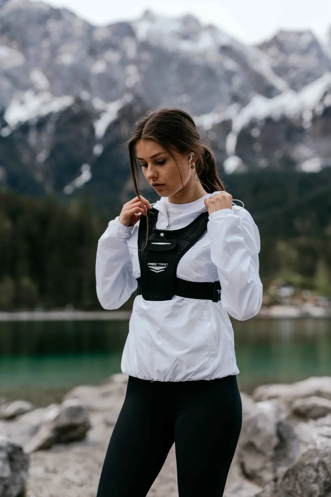 Freetrain – Eine junge Frau in Sportbekleidung steht vor einer Bergkulisse an einem See