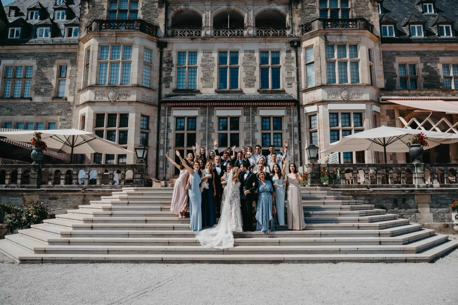 Jana & Murat – Eine Hochzeitsgesellschaft posiert für ein Gruppenfoto auf den Stufen vor einem großen Schloss