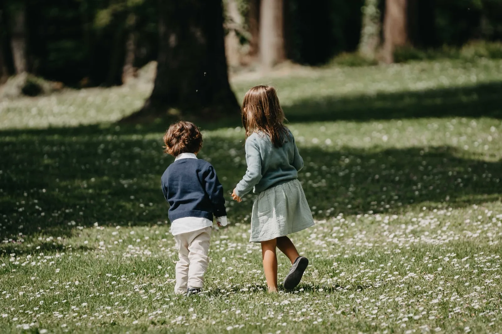 Jessica & Adrian – Zwei kleine Kinder laufen von hinten fotografiert über eine blühende Wiese am Waldrand