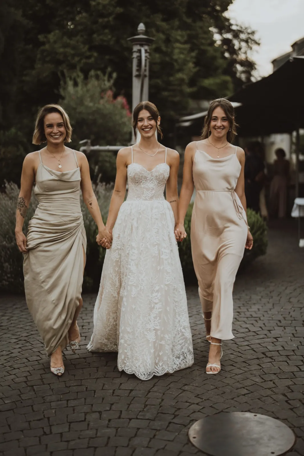 Julia & Chris – Eine Braut läuft Hand in Hand mit ihren beiden Brautjungfern über ein Kopfsteinpflaster
