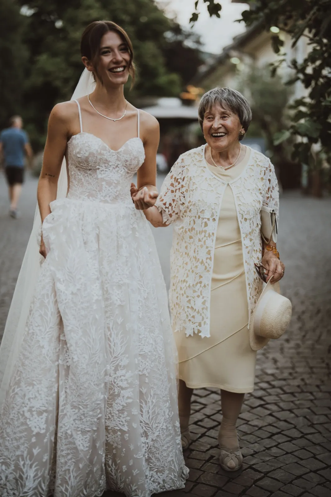 Julia & Chris – Eine Braut im weißen Hochzeitskleid läuft lachend Hand in Hand mit einer älteren Dame