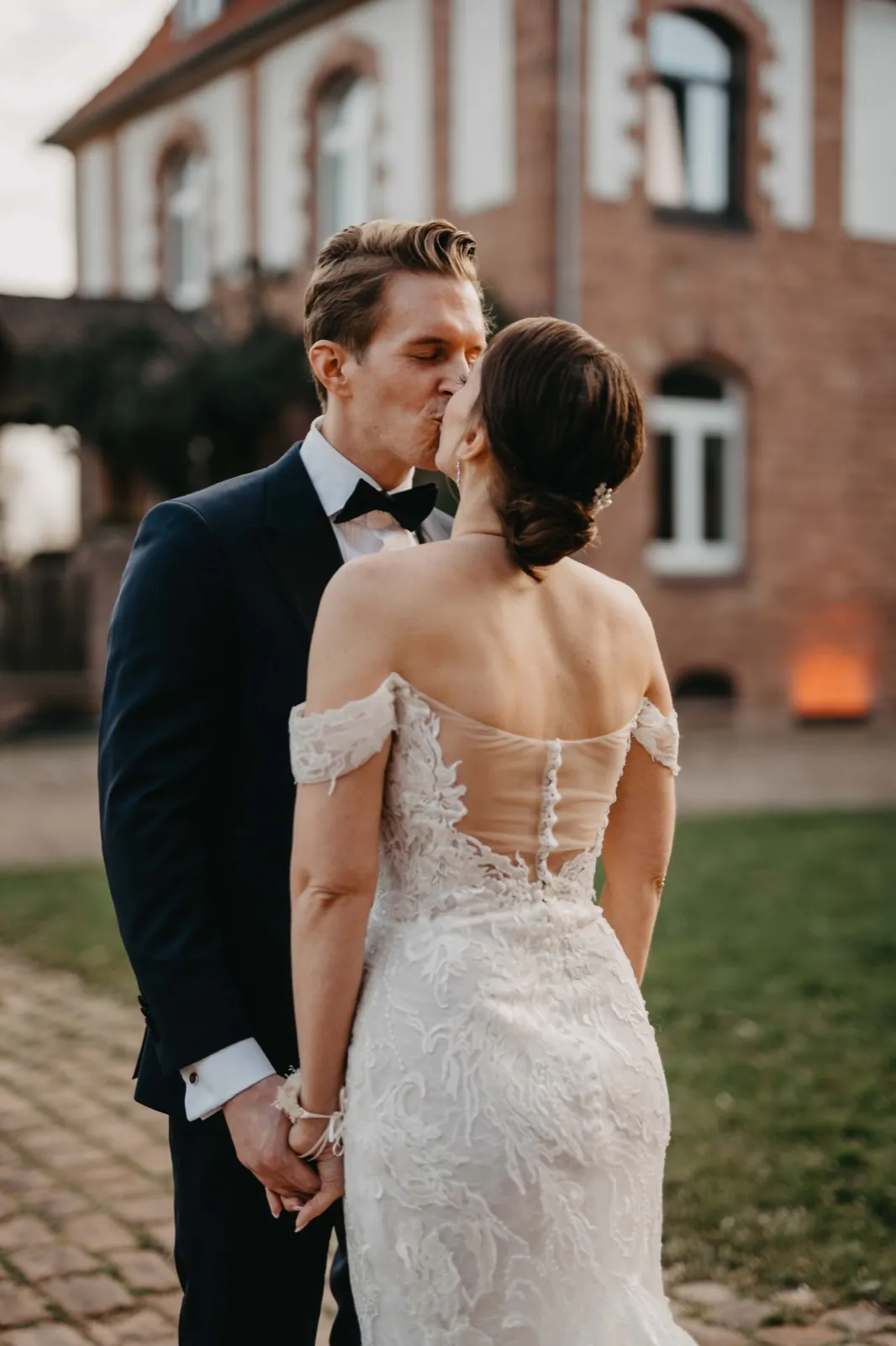 Julia & Florian – Ein Brautpaar küsst sich im Freien vor einem Backsteingebäude