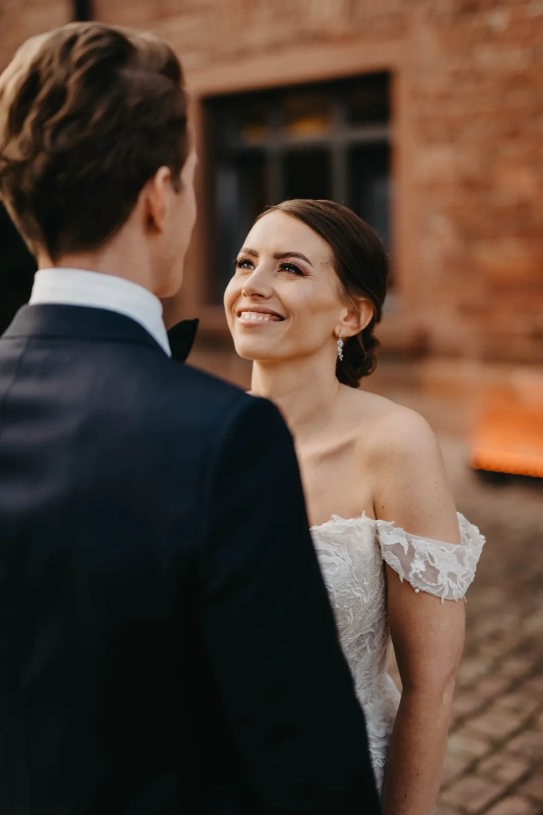 Julia & Florian – Eine Braut blickt lächelnd ihren Bräutigam an, der ihr im Vordergrund gegenübersteht
