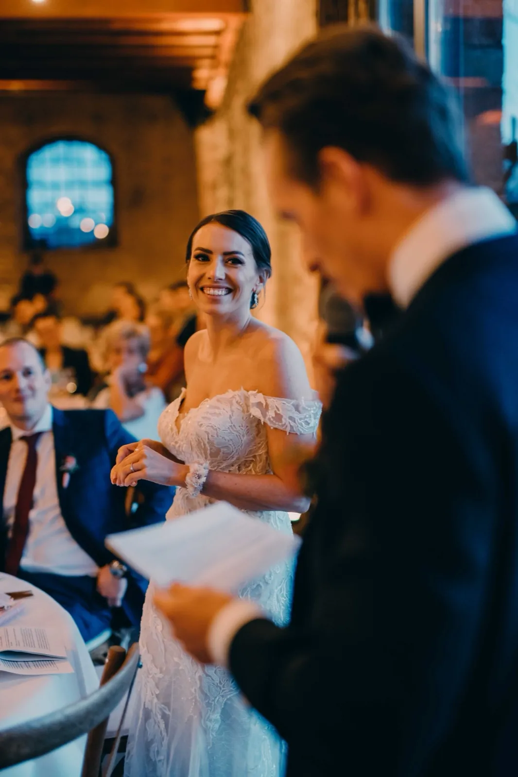 Julia & Florian – Die Braut lächelt glücklich, während im Vordergrund eine Rede gehalten wird