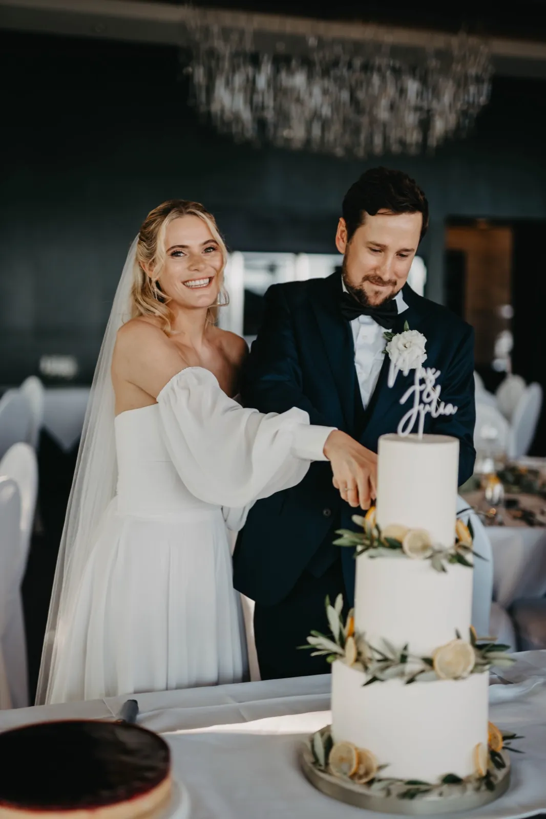 Julia & Max – Ein Brautpaar schneidet gemeinsam die dreistöckige Hochzeitstorte an