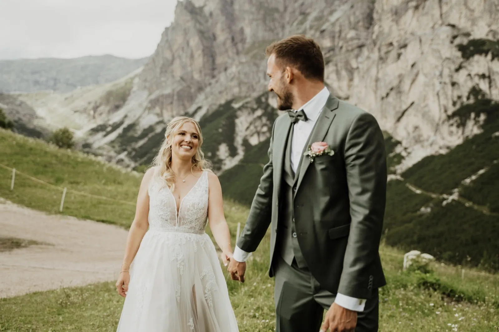 Katrin & Markus – Ein Brautpaar läuft Hand in Hand lächelnd vor einer alpinen Bergkulisse