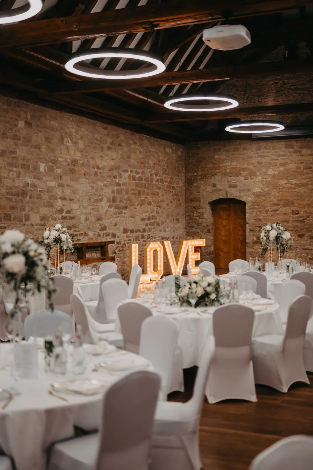 Kristina & Pascal – Festlich gedeckte Tische in einem Saal mit einem leuchtenden LOVE-Schriftzug im Hintergrund