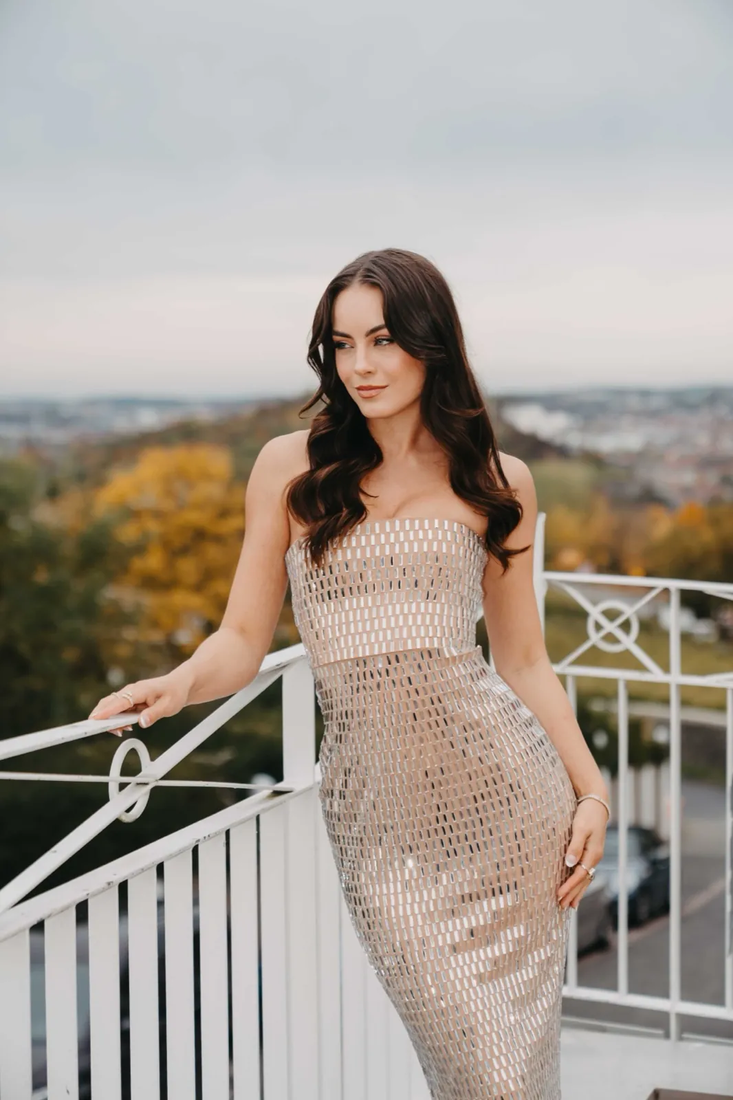 Lara Runarsson – Eine Frau im glitzernden Kleid posiert auf einem Balkon vor herbstlicher Kulisse