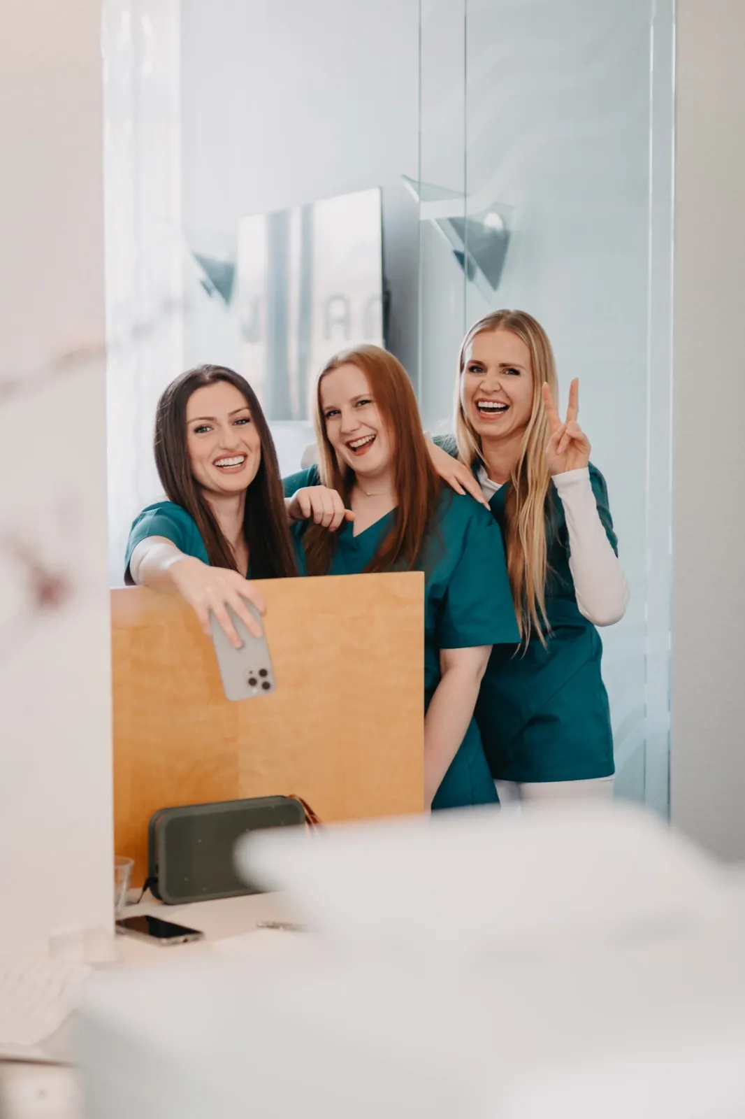 May – Drei Frauen in grüner Arbeitskleidung lächeln fröhlich für ein Selfie im Spiegel