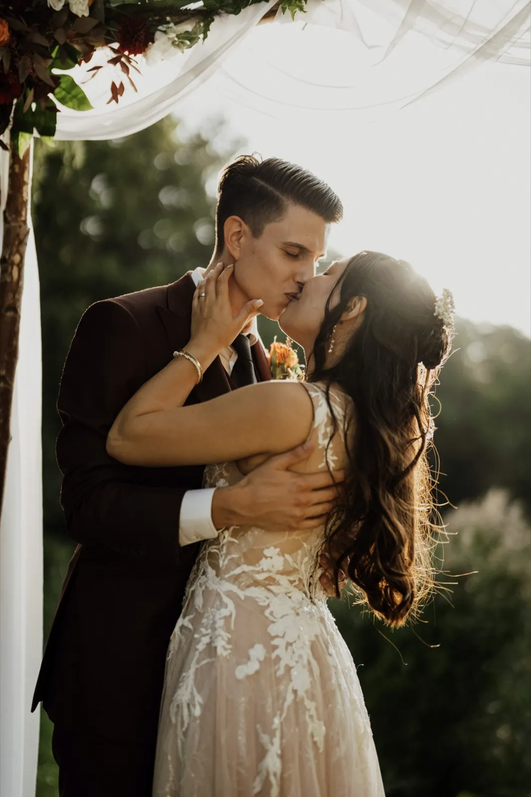 Marie & Thomas – Ein Brautpaar küsst sich innig im warmen Gegenlicht während ihrer Hochzeit im Freien