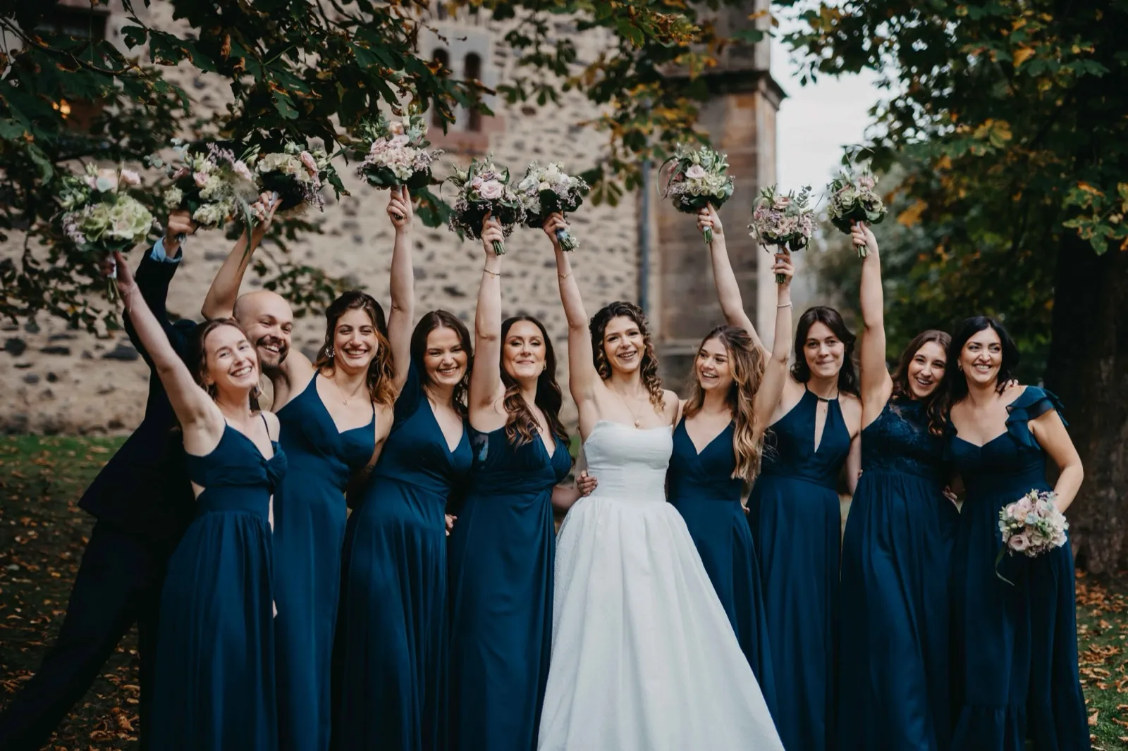 Mia & Clemens – Eine Braut im weißen Kleid feiert draußen mit ihren Brautjungfern in dunkelblauen Kleidern