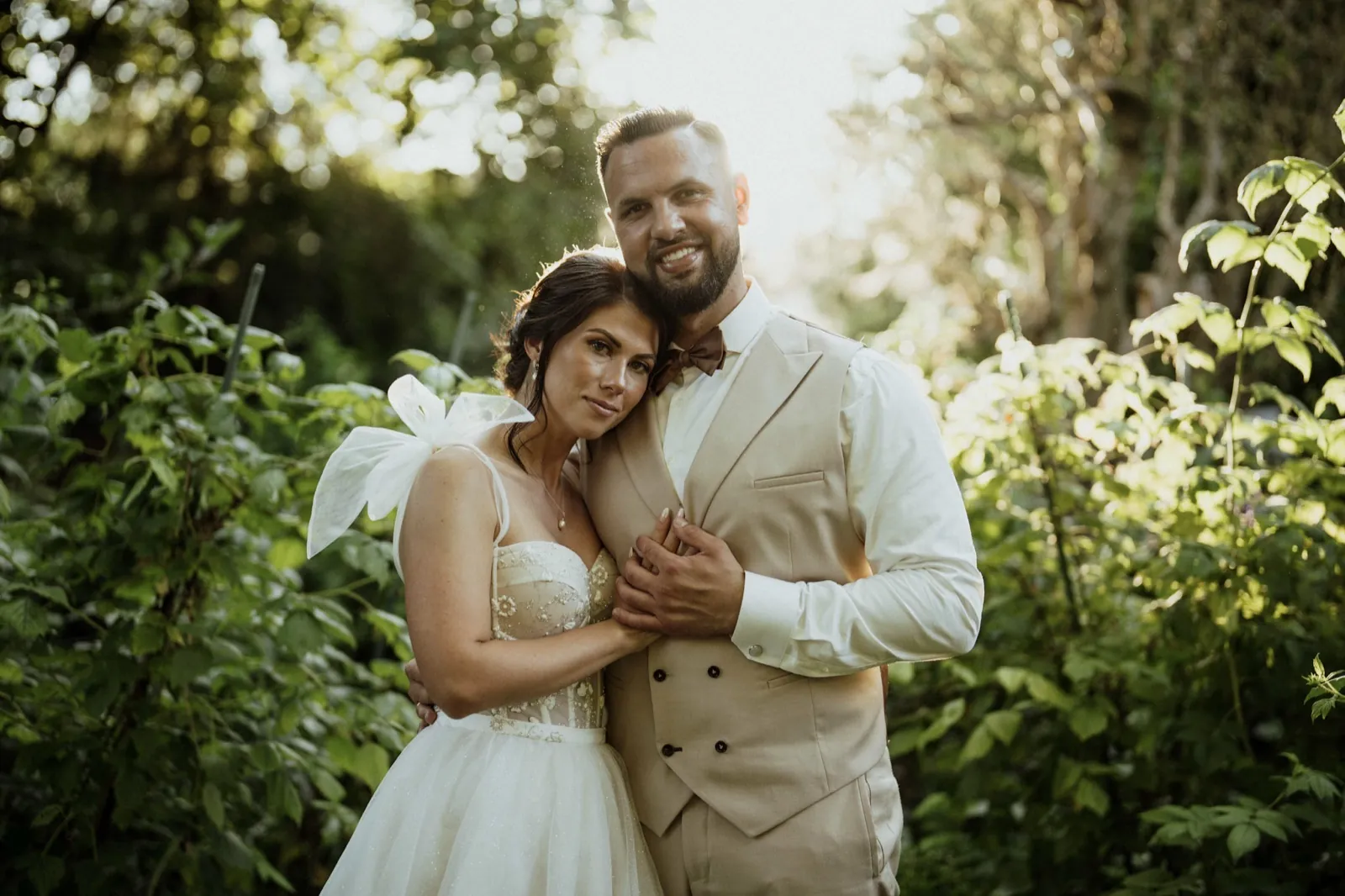 Nadine & Raphael – Ein Brautpaar posiert lächelnd im Gegenlicht im Freien