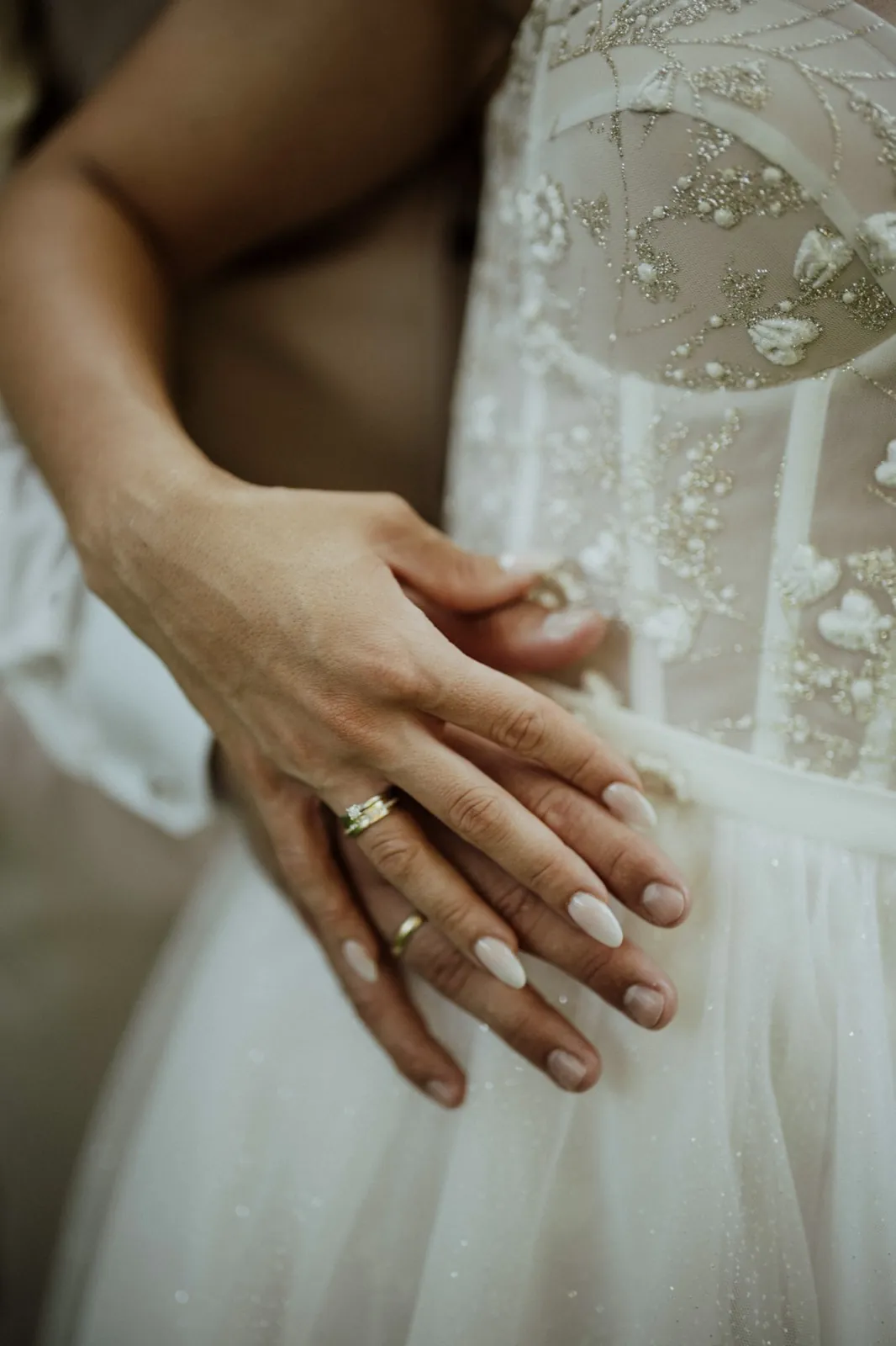 Nadine & Raphael – Nahaufnahme der Hände des Brautpaars mit Eheringen auf dem Hochzeitskleid