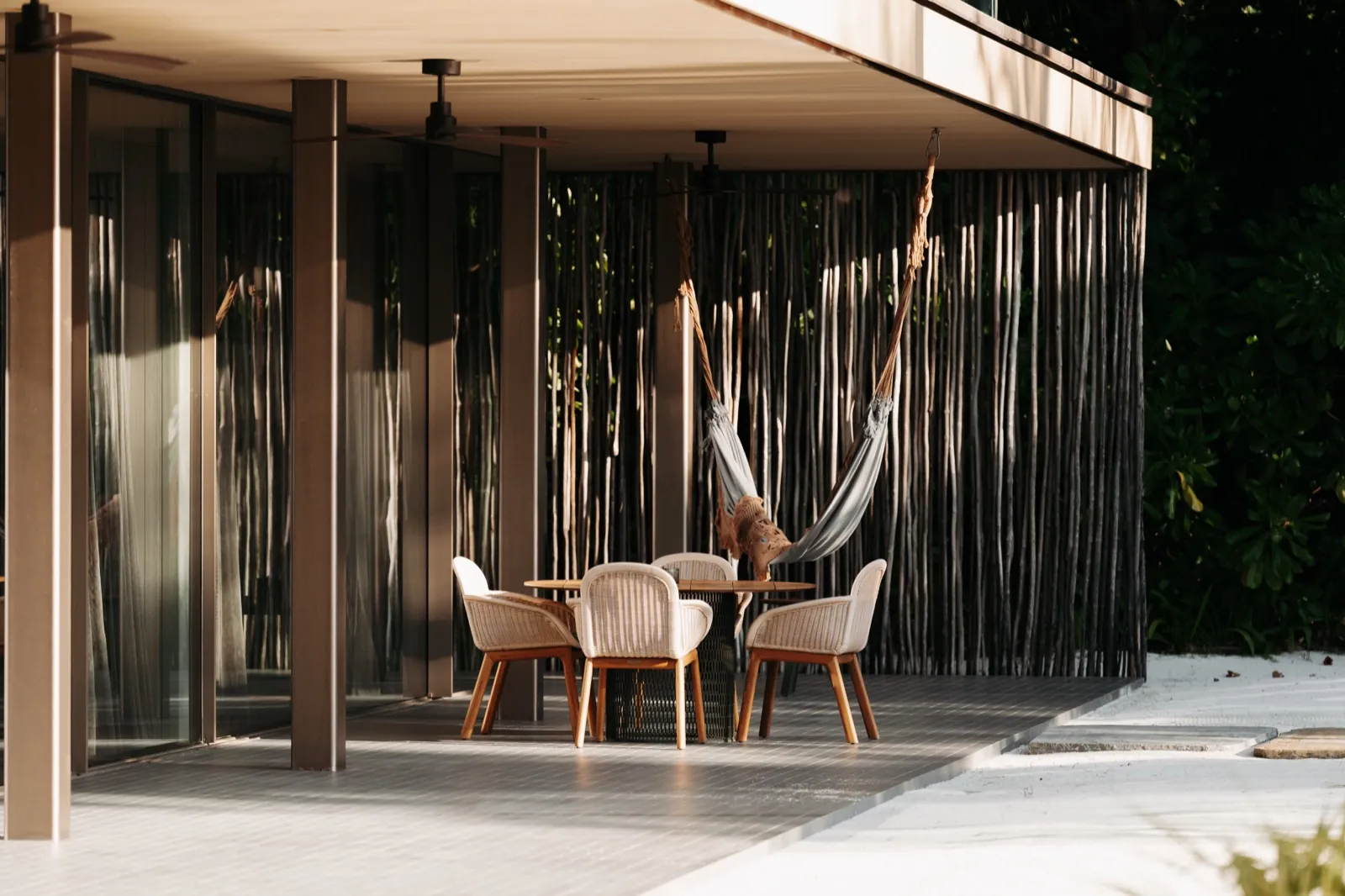 Patina Maldives – Eine moderne Terrasse mit einem Tisch, vier Stühlen und einer Hängematte am Strand