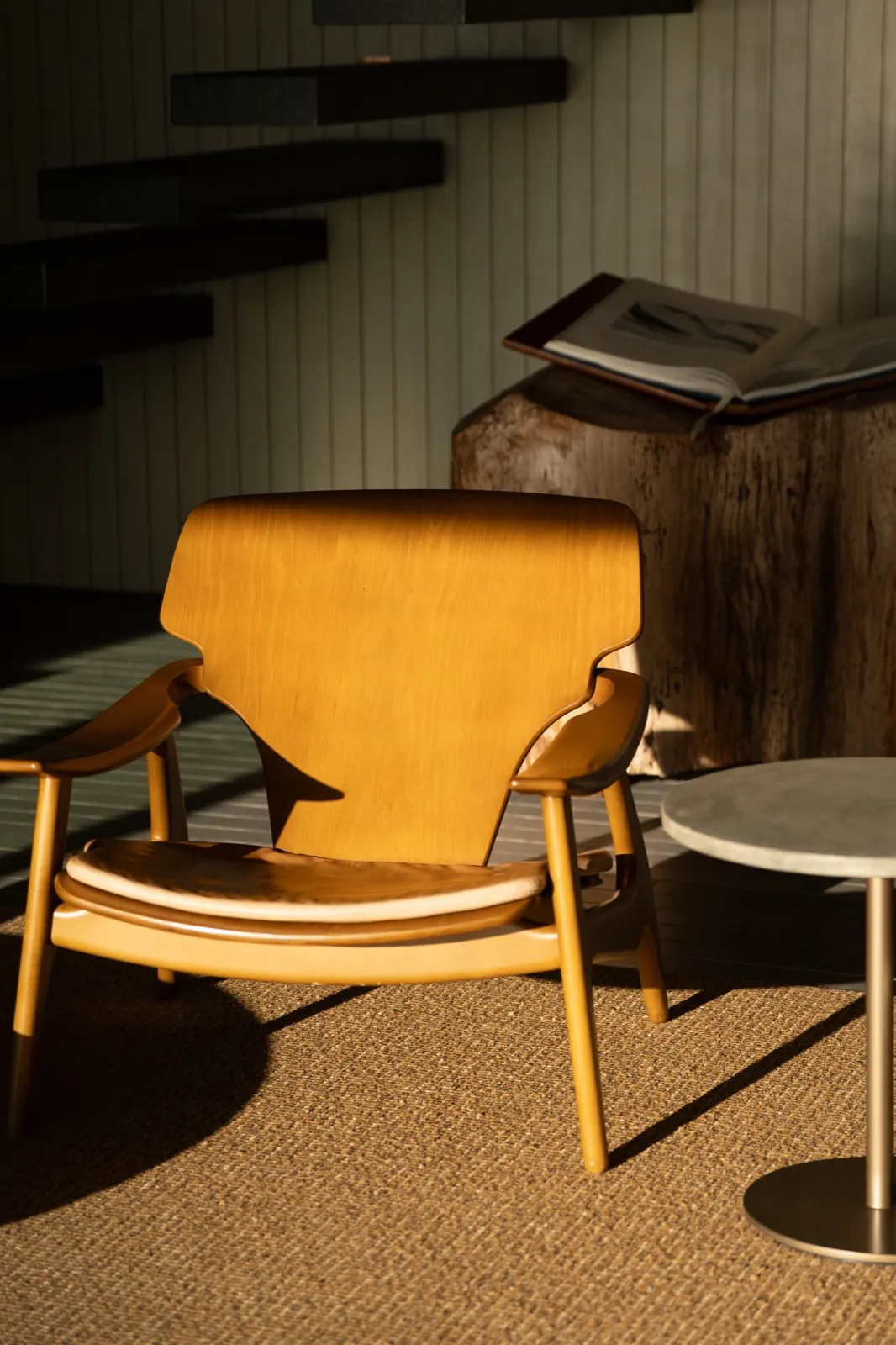 Patina Maldives – Ein hölzerner Designer-Sessel steht im warmen Sonnenlicht in einem modern gestalteten Innenraum