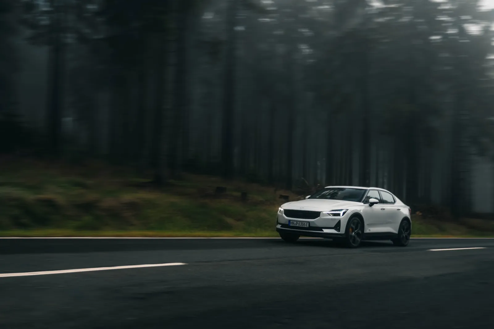 Polestar – Ein weißes Auto fährt auf einer Straße durch einen nebligen Wald