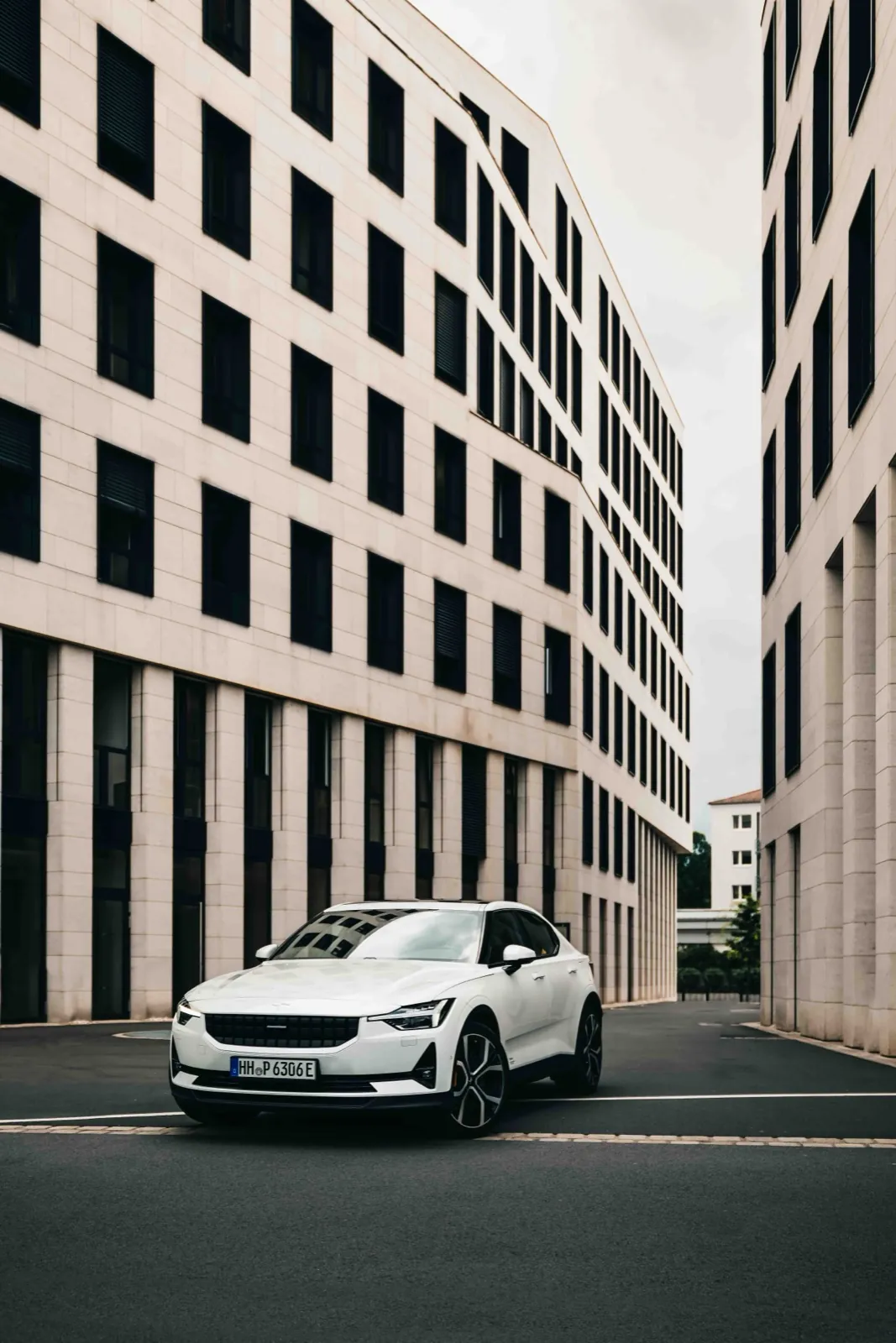 Polestar – Ein weißes Elektroauto steht auf einer Straße zwischen modernen, hellen Bürogebäuden