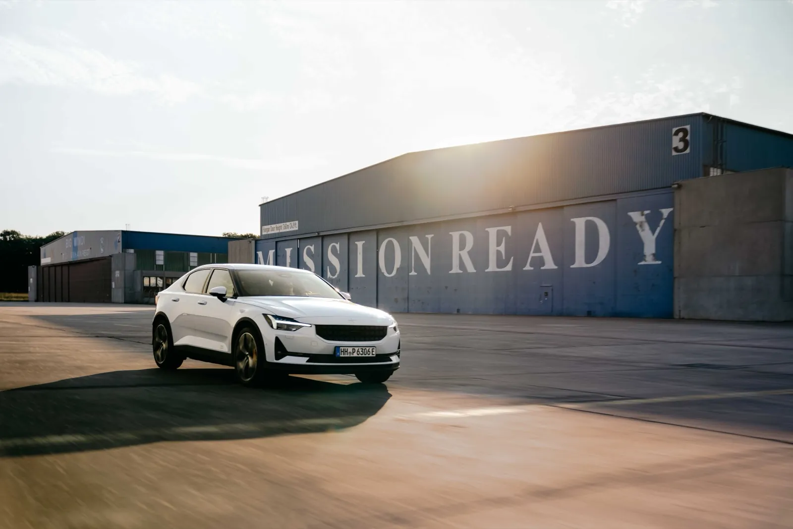 Polestar – Ein weißes Elektroauto fährt im Abendlicht auf einem Flugplatz vor einer Halle