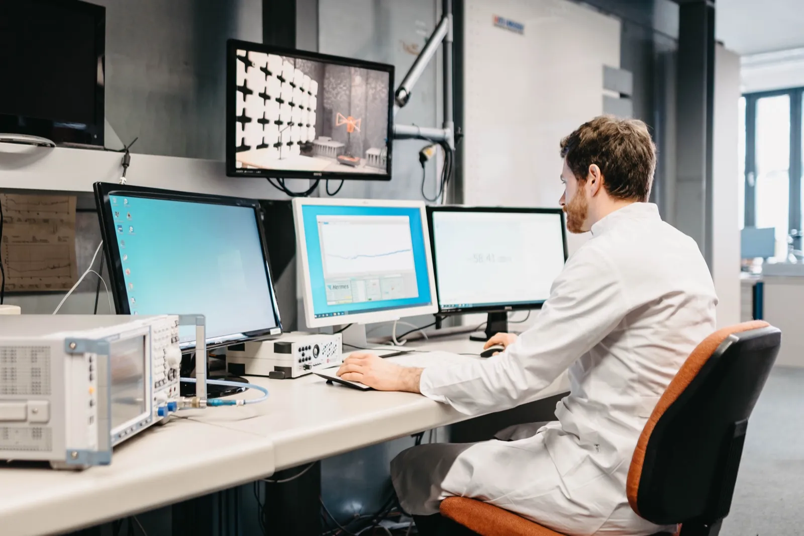 QIMA – Ein Wissenschaftler im weißen Kittel arbeitet an mehreren Computerbildschirmen in einem Labor