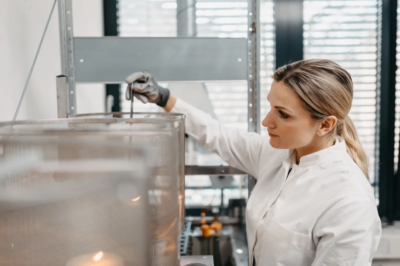 QIMA – Eine Wissenschaftlerin im weißen Laborkittel arbeitet konzentriert an einer Laborapparatur