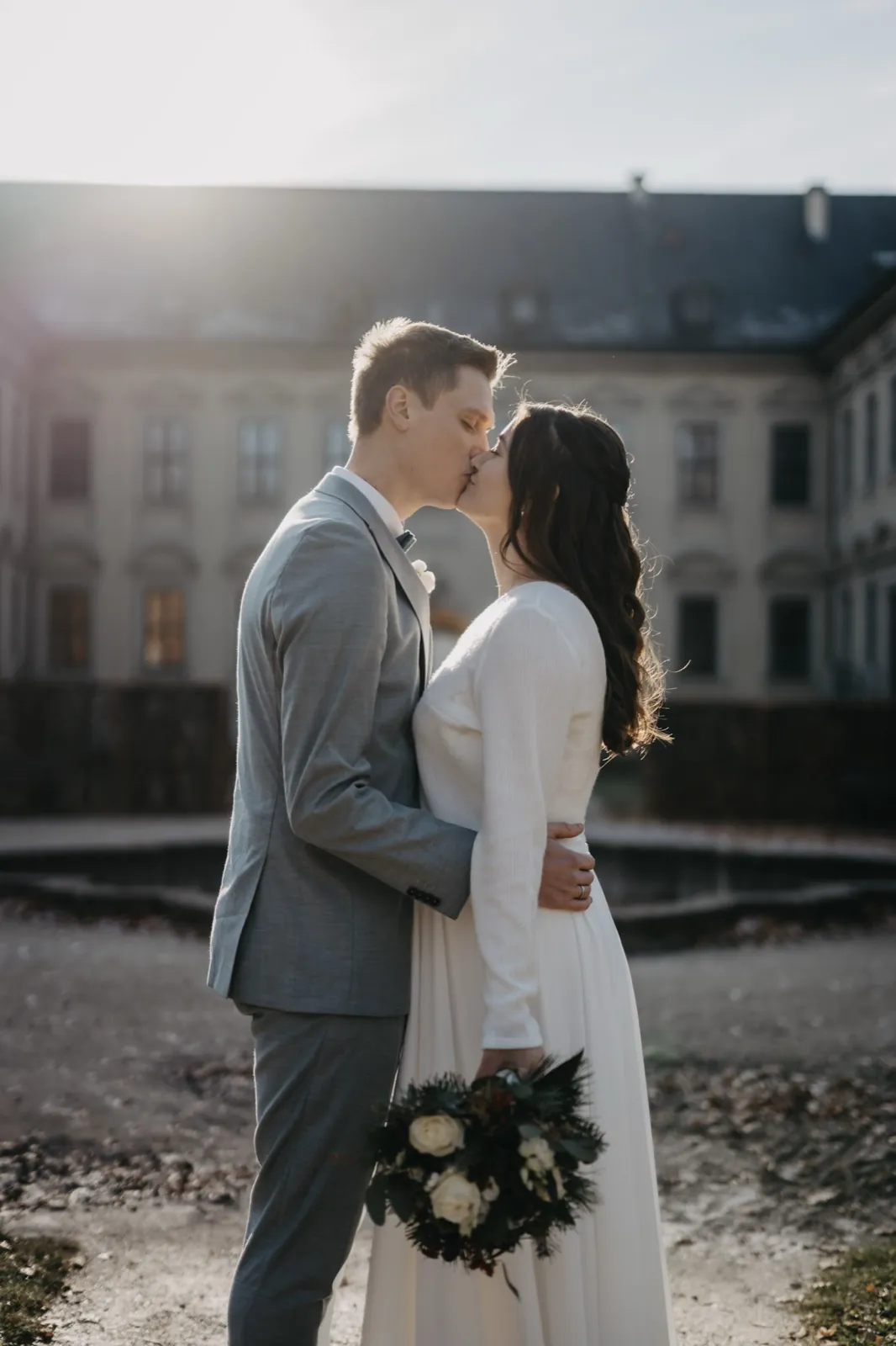 Sophie & Mirko – Ein Brautpaar küsst sich im Gegenlicht vor einem historischen Gebäude