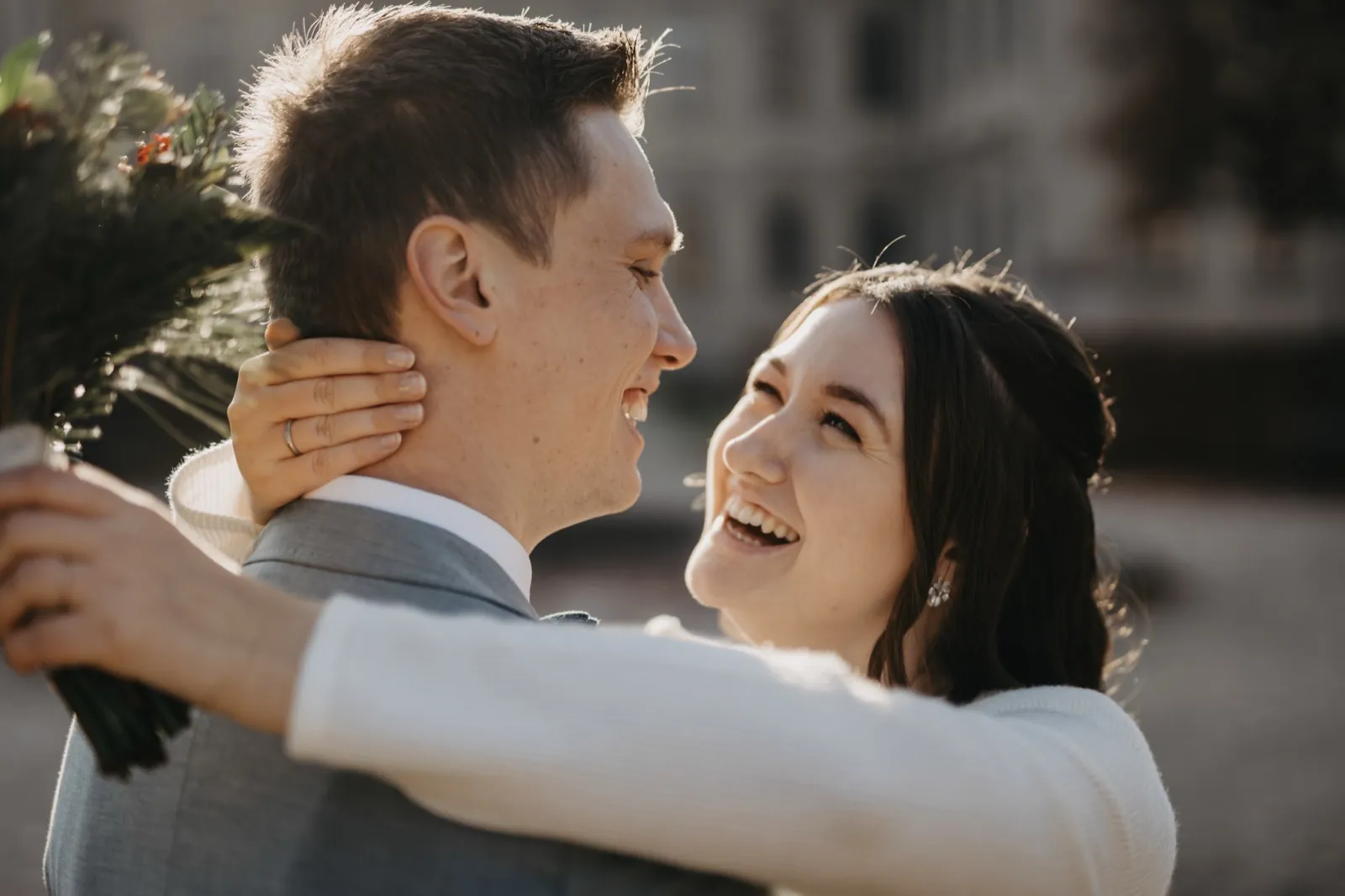 Sophie & Mirko – Ein lachendes Brautpaar umarmt sich im warmen Gegenlicht im Freien