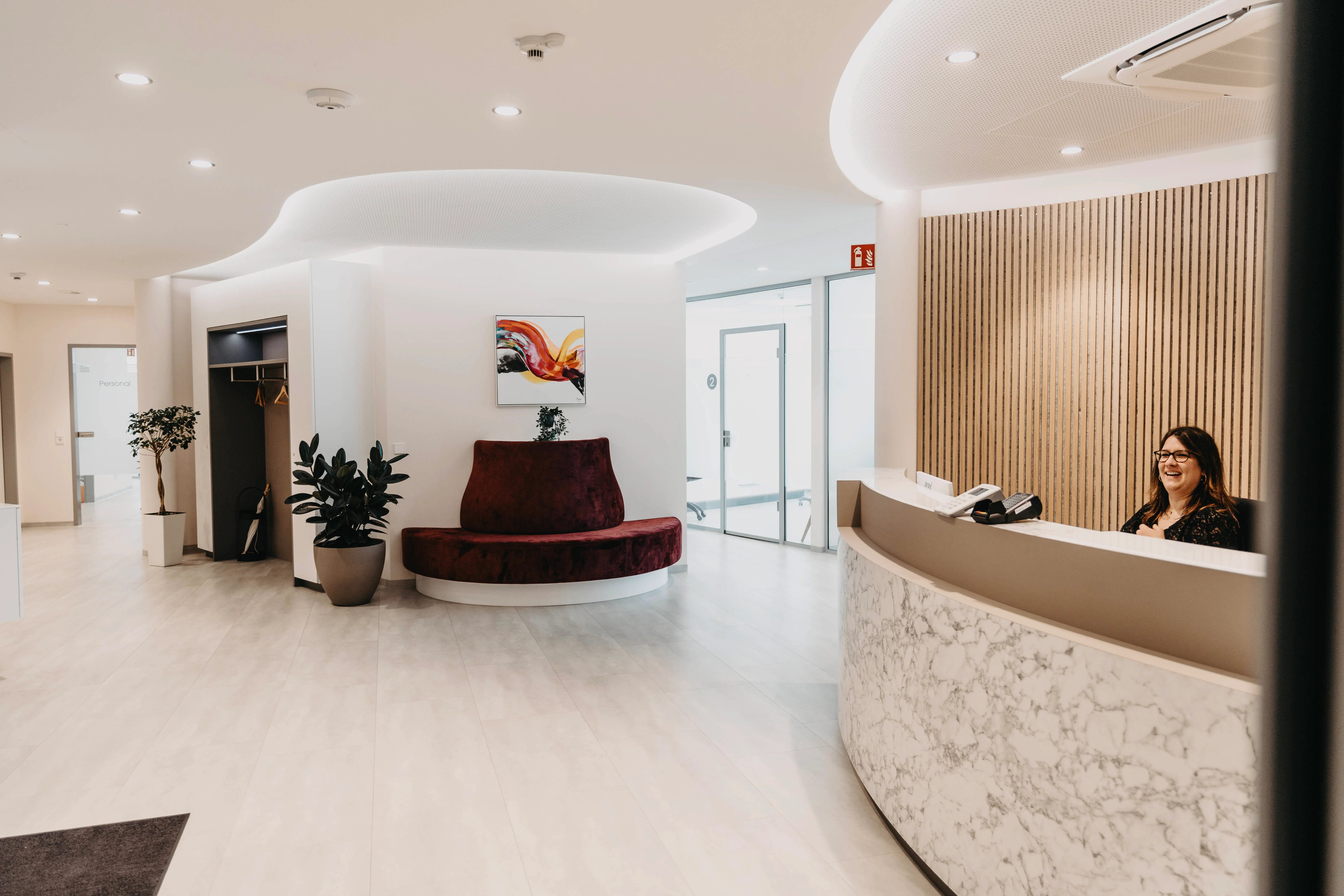 ZahnZentrum 79 – Ein moderner Empfangsbereich mit einer lächelnden Mitarbeiterin hinter dem Tresen und einer roten Sitzbank