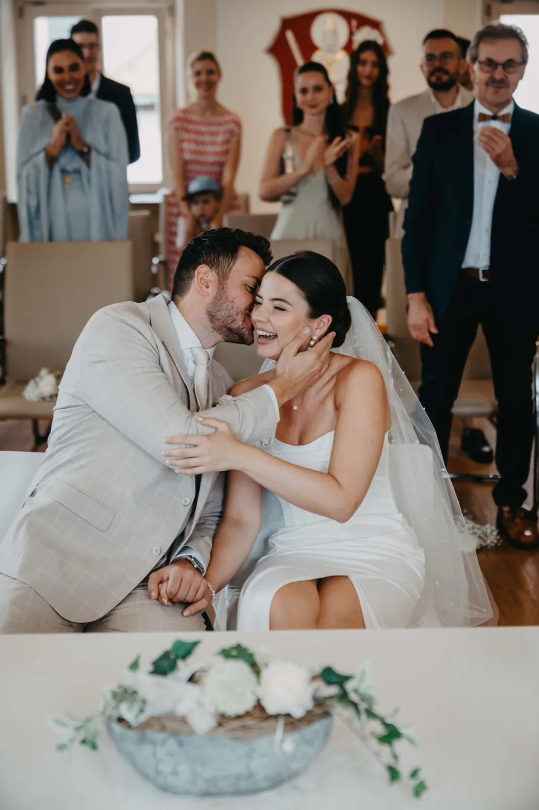 Verena & Rafael – Ein Bräutigam flüstert seiner lachenden Braut während der Hochzeitszeremonie etwas ins Ohr