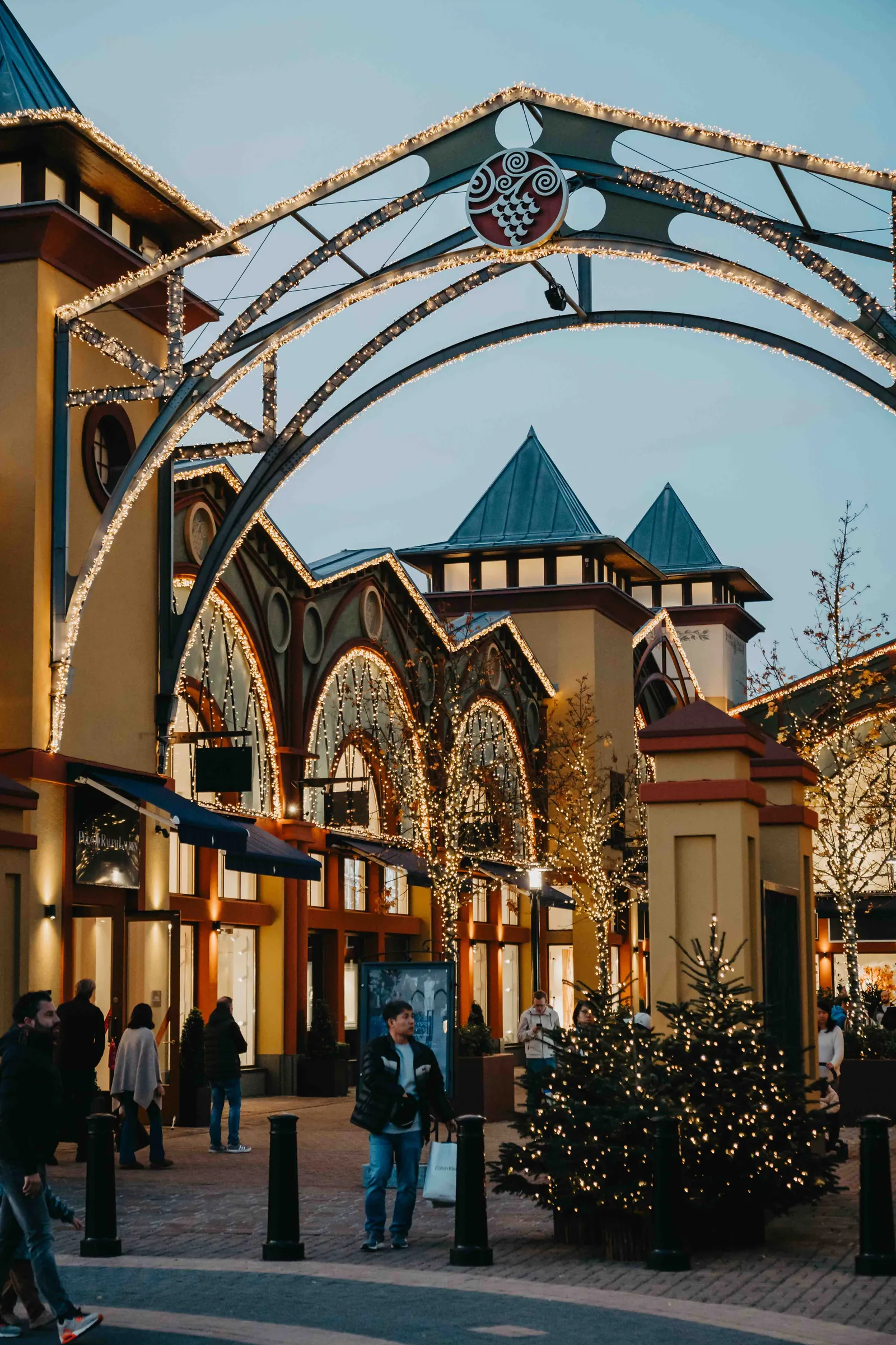 Wertheim Village – Ein weihnachtlich beleuchtetes Einkaufszentrum im Freien mit Besuchern am Abend