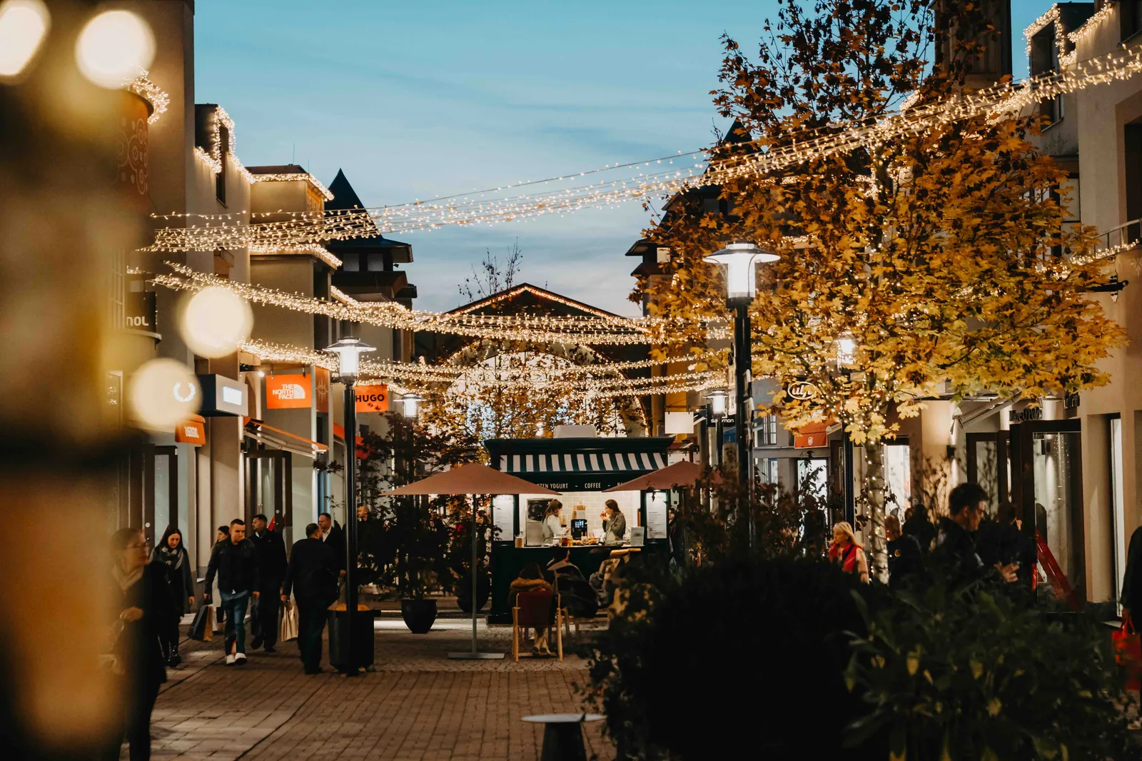 Wertheim Village – Eine beleuchtete Einkaufsstraße am Abend mit Lichterketten und Fußgängern